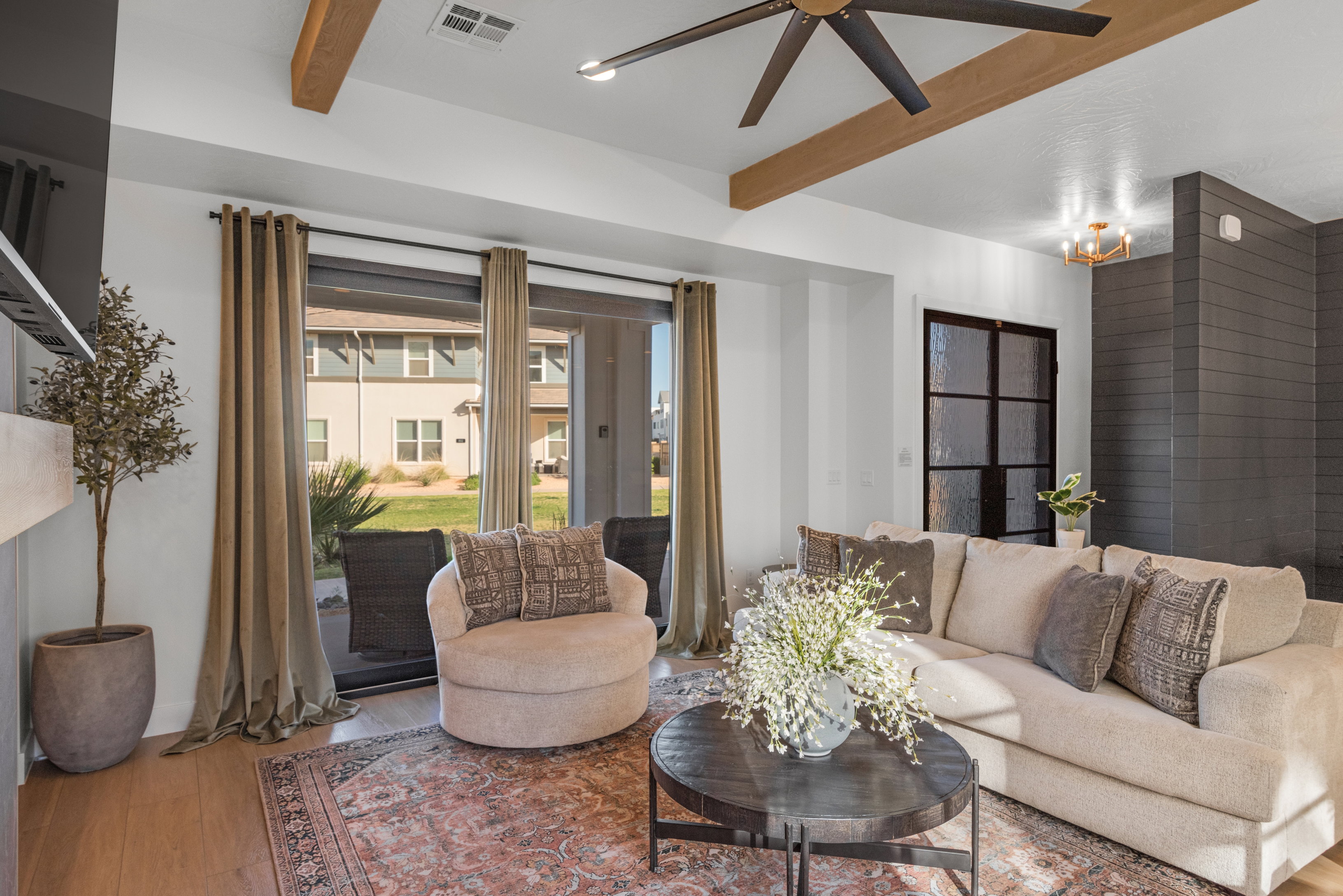 Living area featuring wood-finish flooring, a contemporary ceiling fan, exposed wood beams, a dark shiplap accent wall, and a black framed glass door
