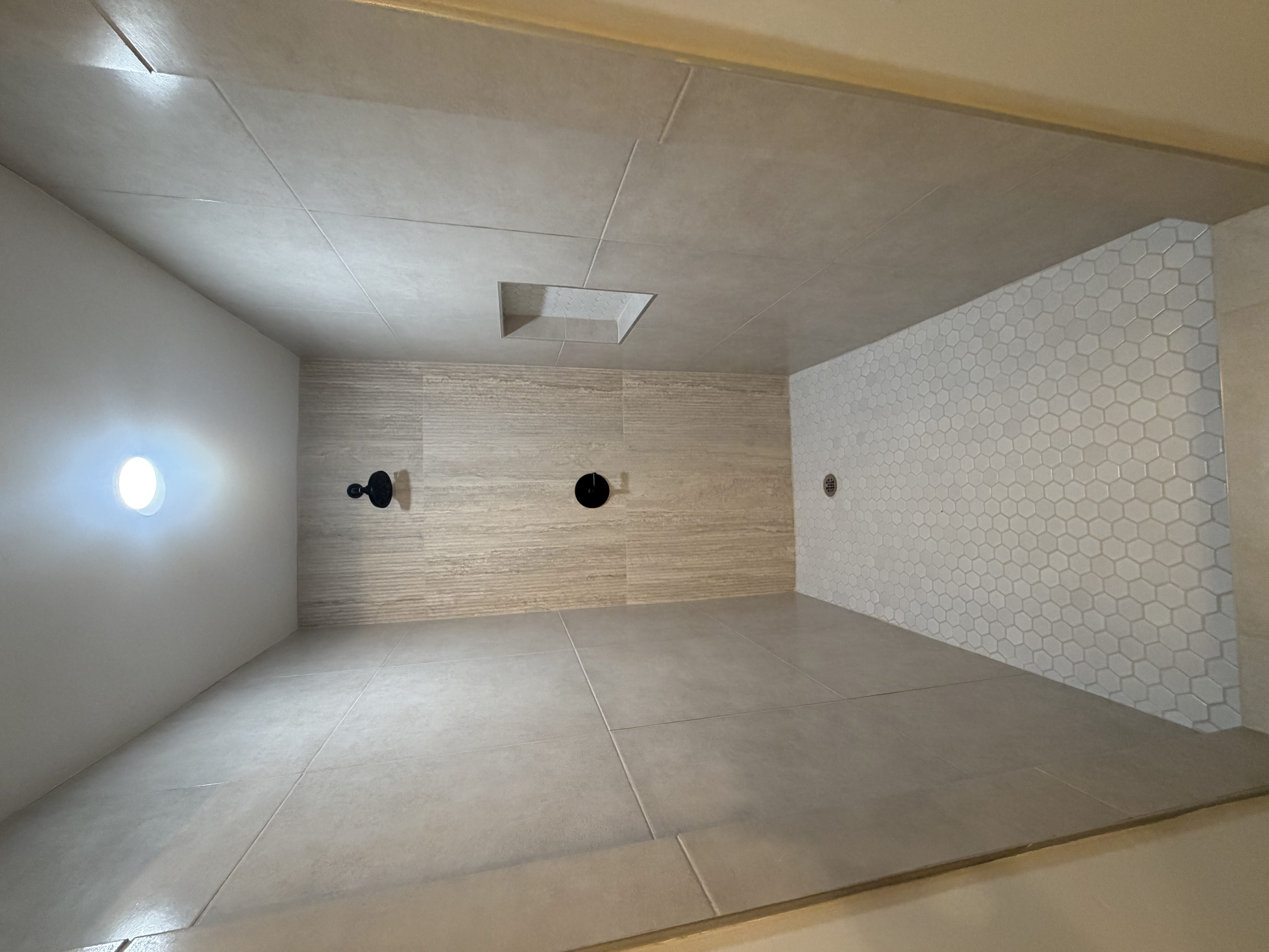 Master bathroom. Walk-in shower with hexagonal tile flooring, vertically stacked tile surround, built-in shelving, matte black fixtures, and recessed lighting