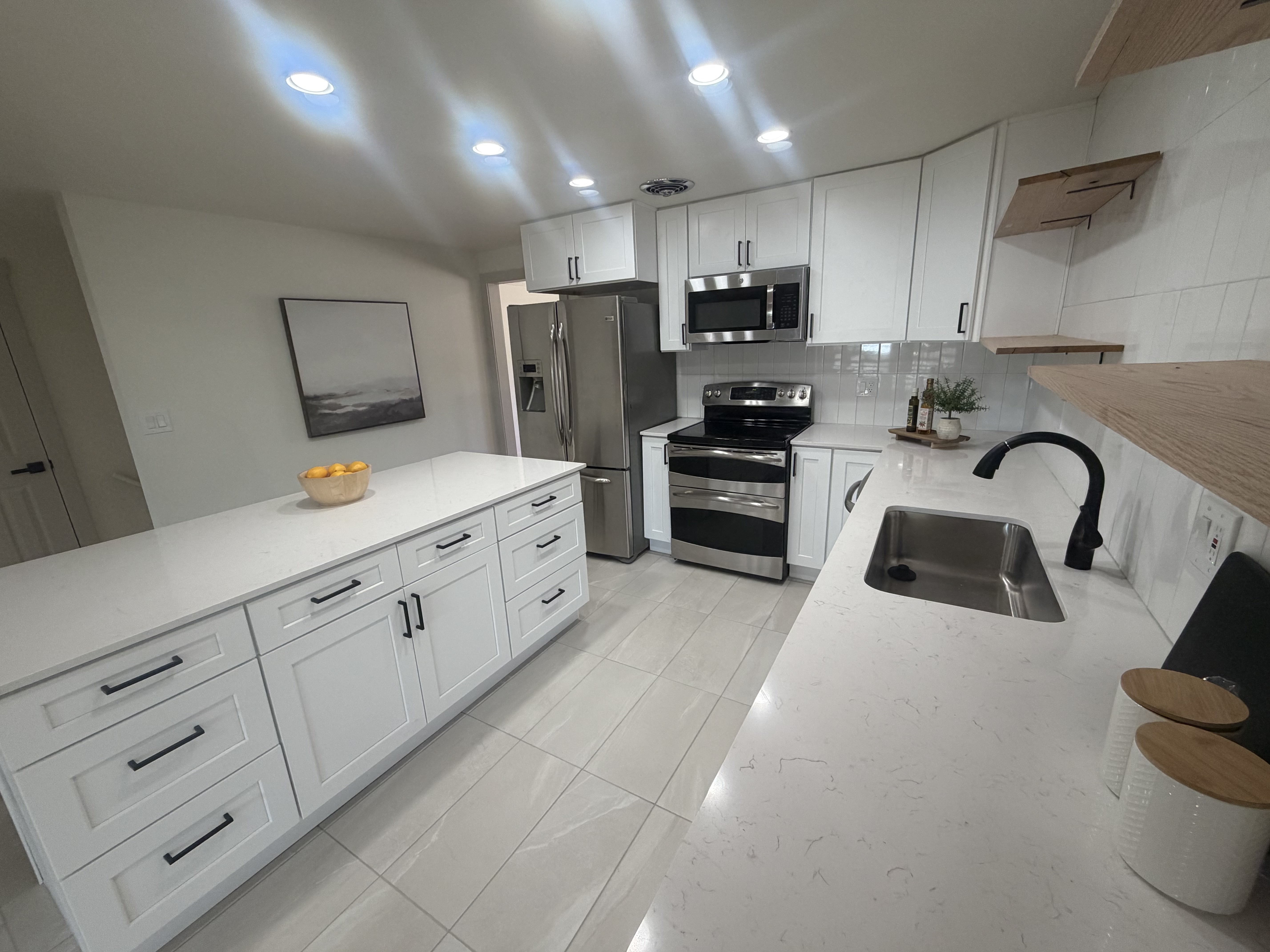 Bright kitchen featuring a large center island with integrated storage, white shaker-style cabinetry, stainless steel appliances, white subway tile backsplash, and light-toned tile flooring