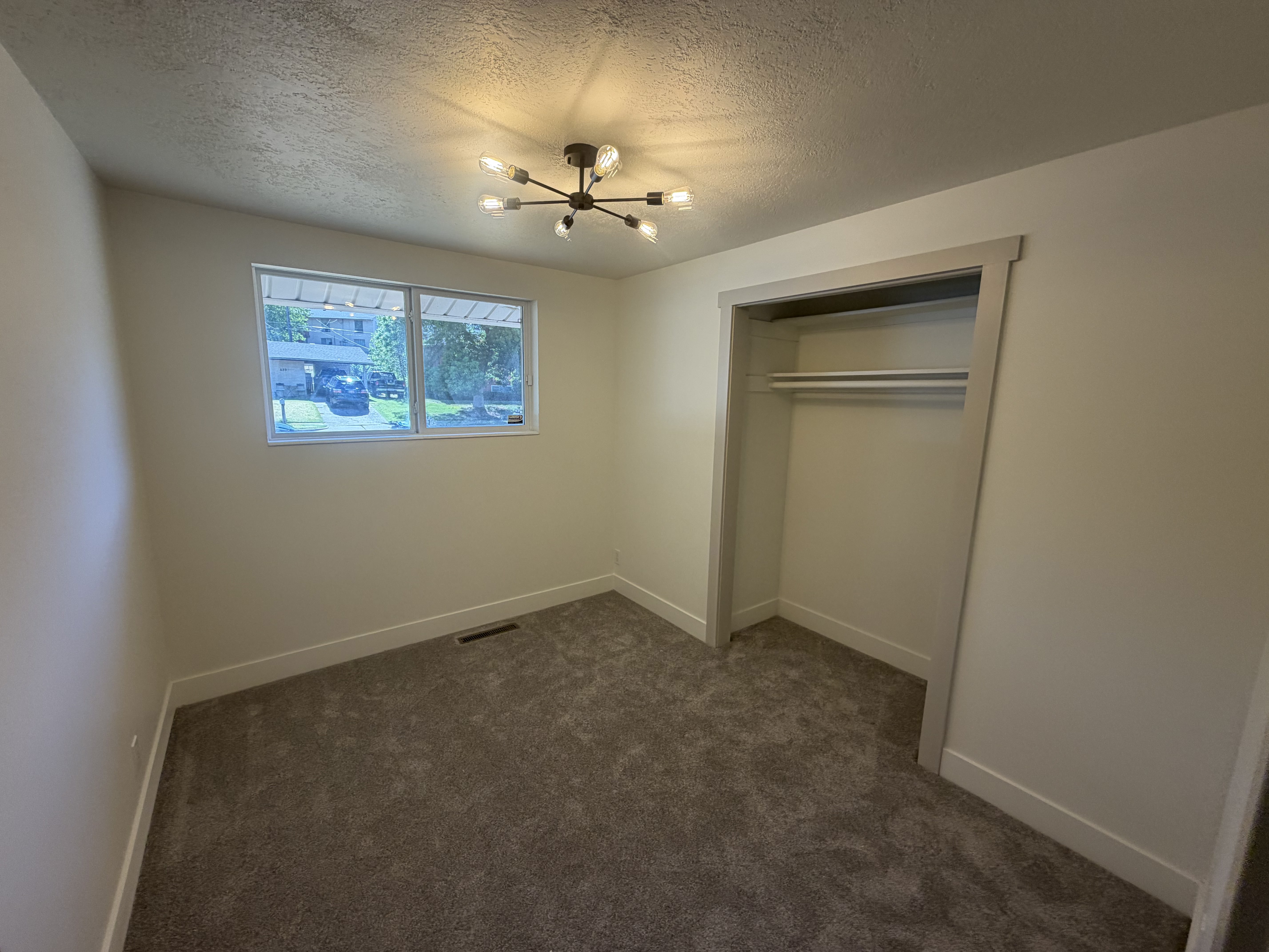 Bedroom 3. Bedroom featuring plush carpet flooring, a contemporary sputnik-style ceiling light fixture, a window with exterior visibility, a built-in closet with shelving and hanging rods, and perimeter base molding