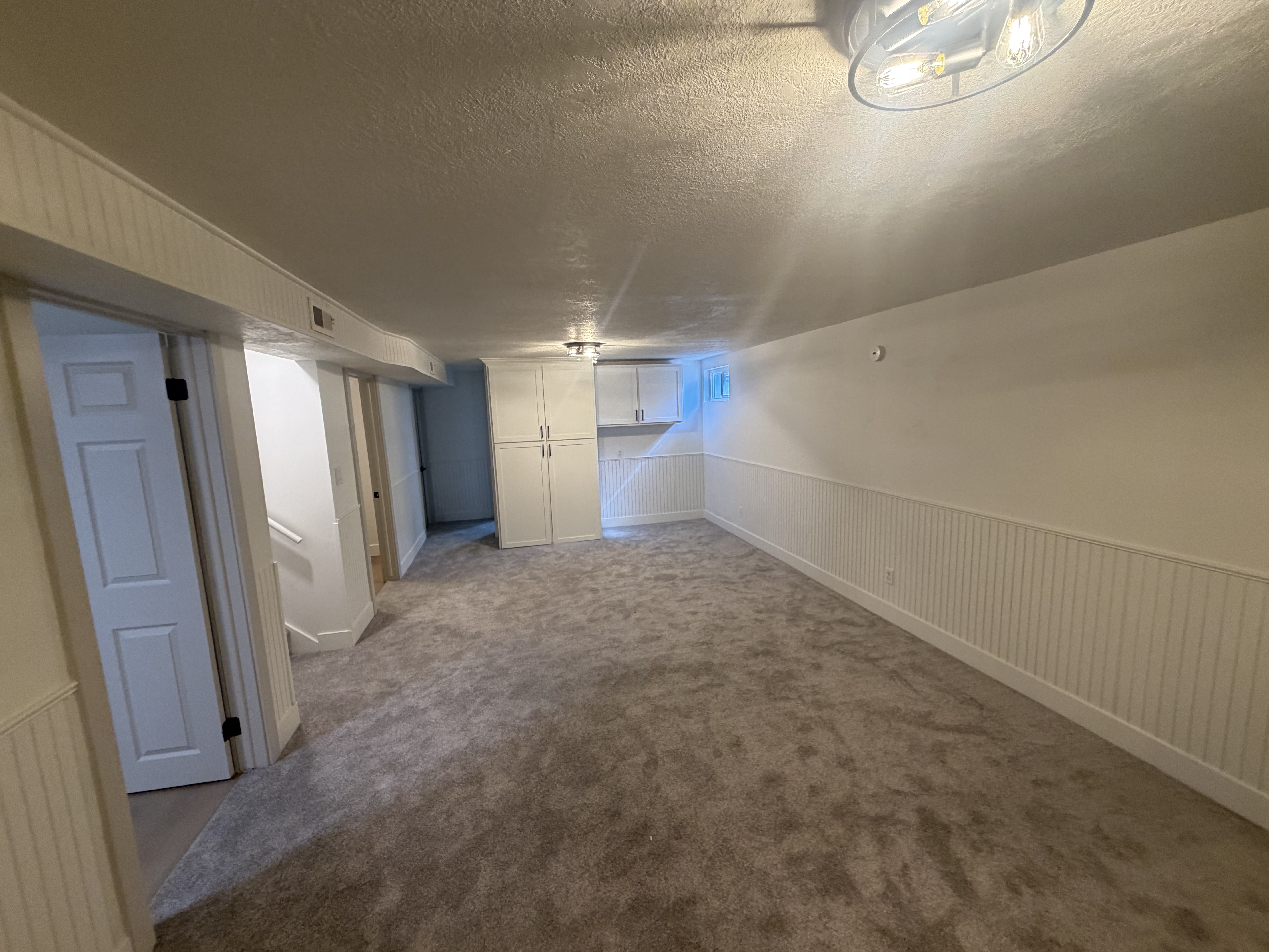 Spacious room featuring gray textured carpeting, white beadboard wainscoting, and white painted walls