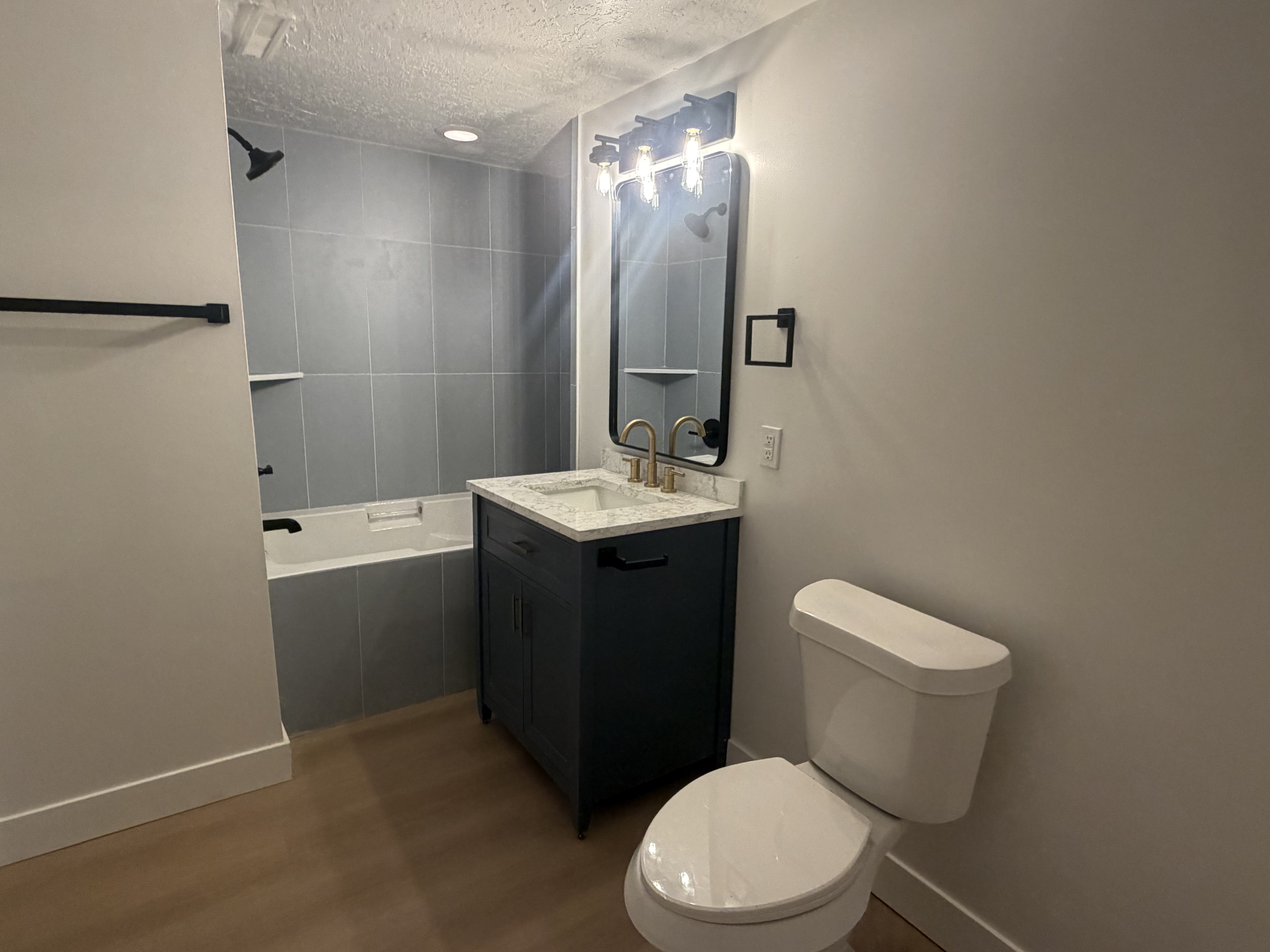 Basement level, full bathroom. Contemporary bathroom featuring a dark blue vanity with a light-toned countertop, a rectangular mirror, and a three-light fixture