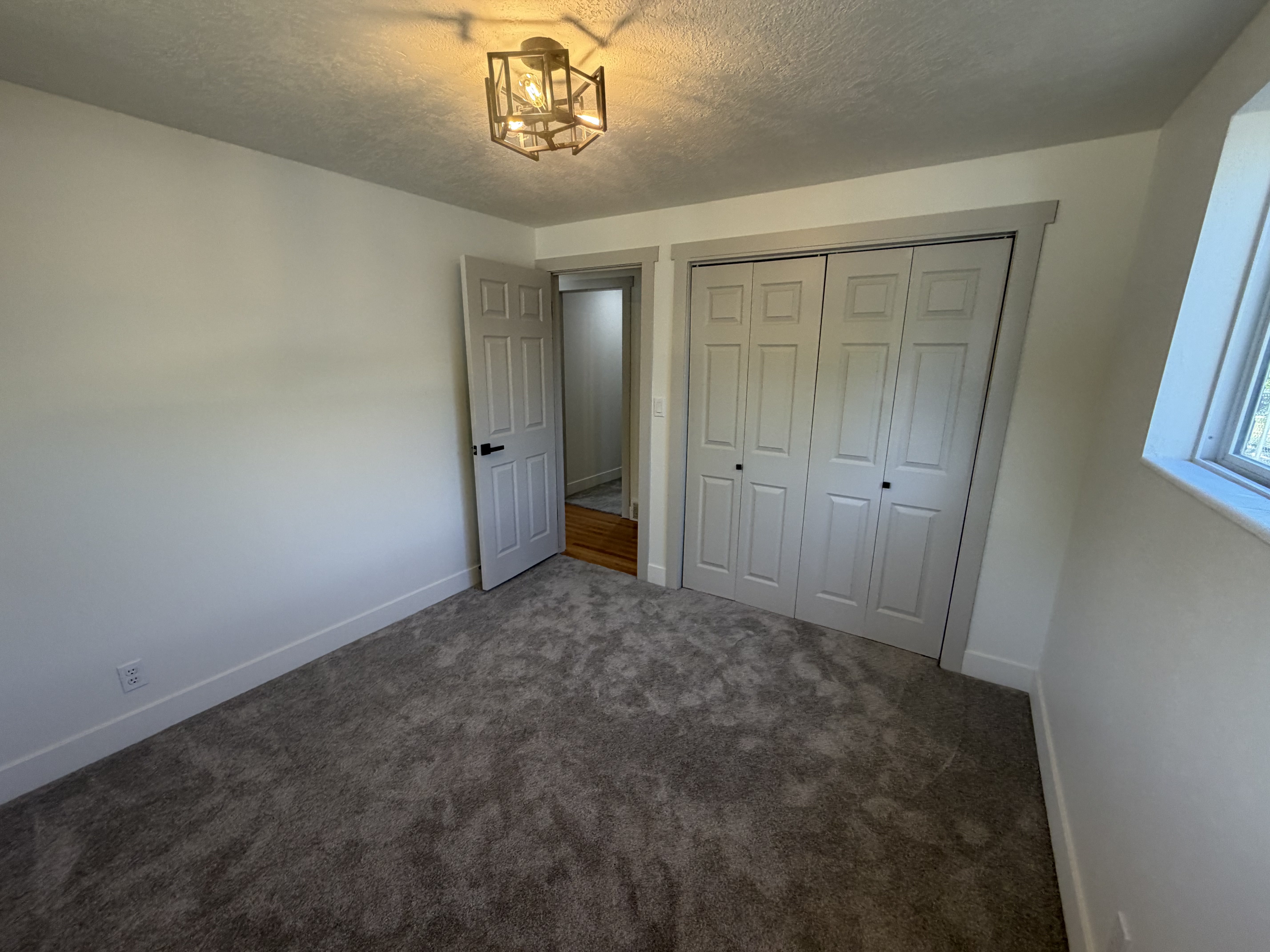 Bedroom 4. Room featuring neutral wall paint, gray carpet, a two-panel bifold closet, a window, and an industrial-style ceiling light fixture