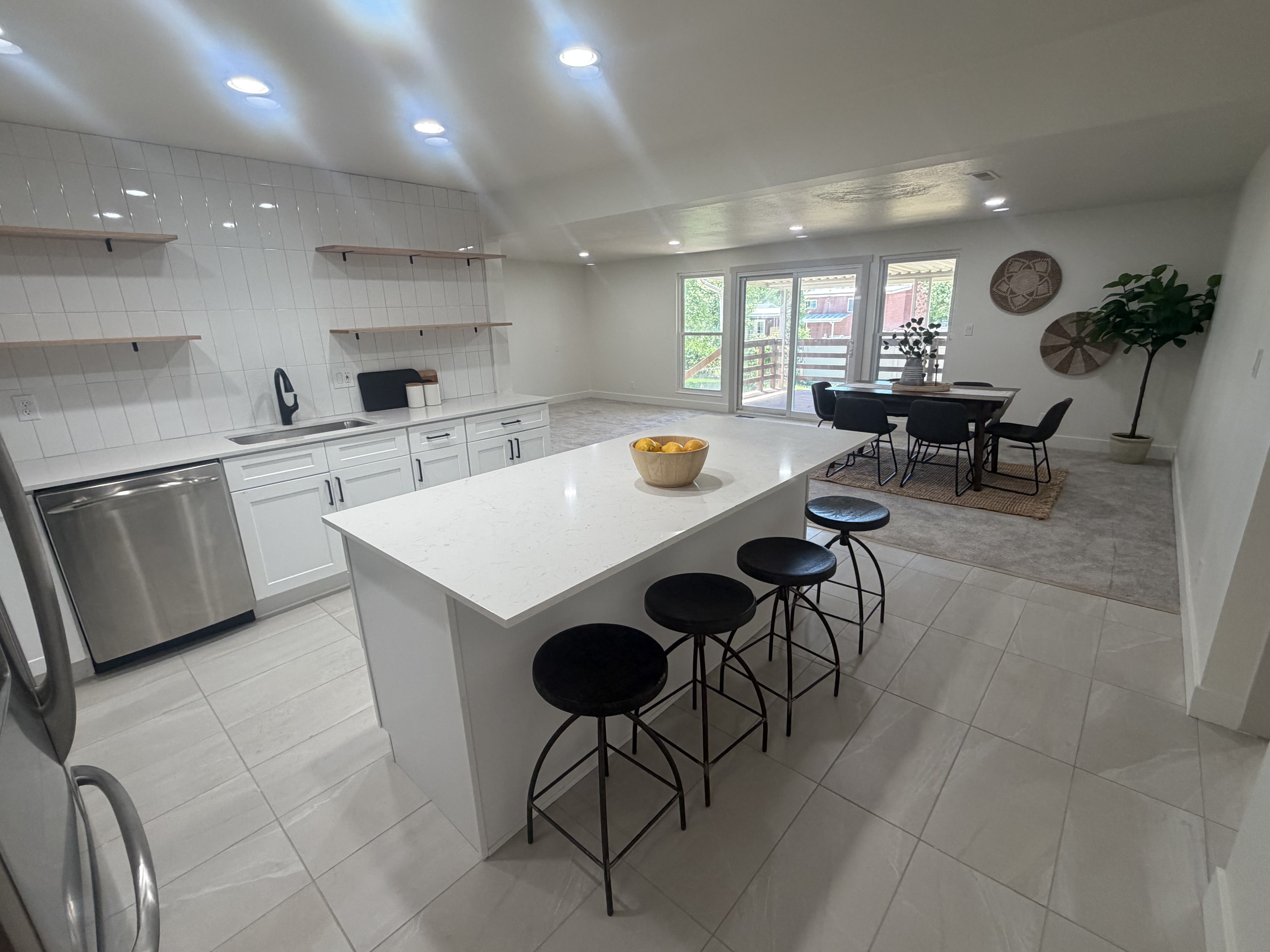 Contemporary kitchen featuring a large center island with a stone-finish countertop, stainless steel appliances, white cabinetry, and a subway tile backsplash