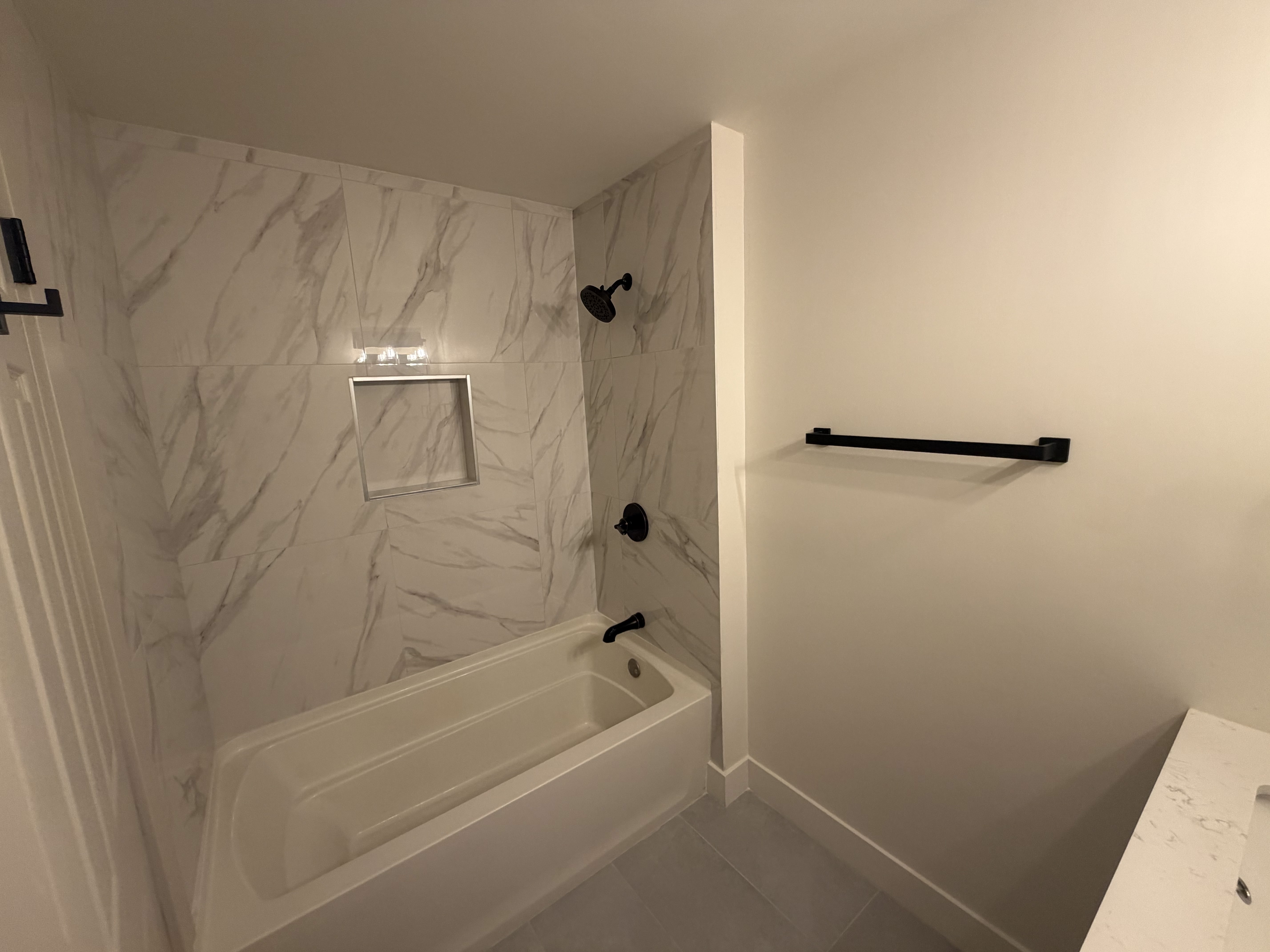 Main level, full bathroom. Bathtub and shower combination featuring large format marble-look tile surround with a built-in niche