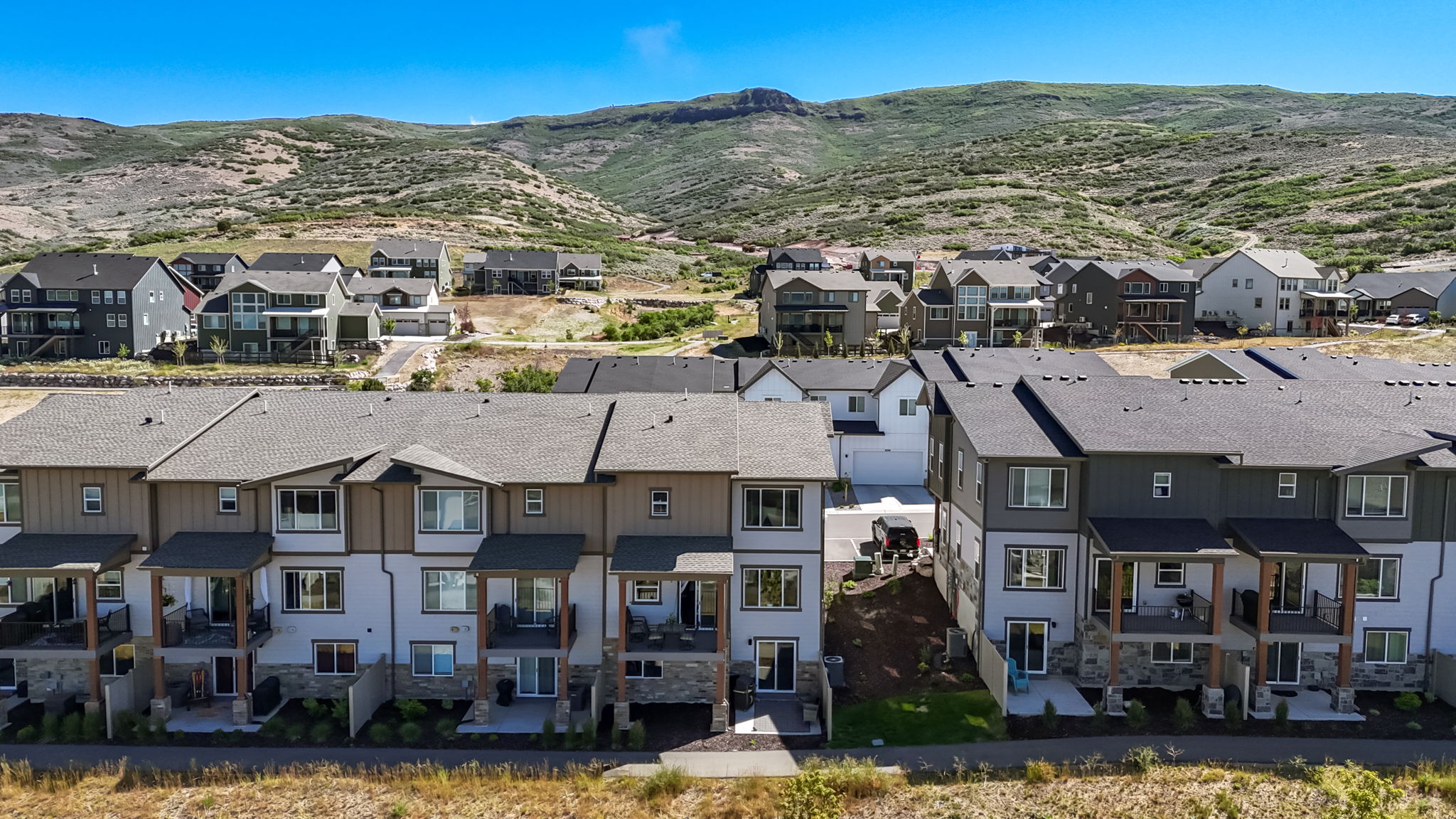 Modern townhome development with multi-level residences, private balconies, stone accents, durable siding, and a mountain backdrop
