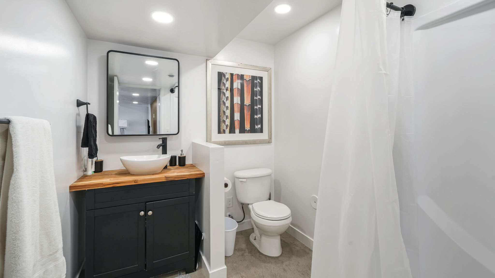 Full bathroom featuring a dark wood-finish vanity with a white vessel sink, a coordinating black-framed mirror, a toilet, and a shower with a white enclosure