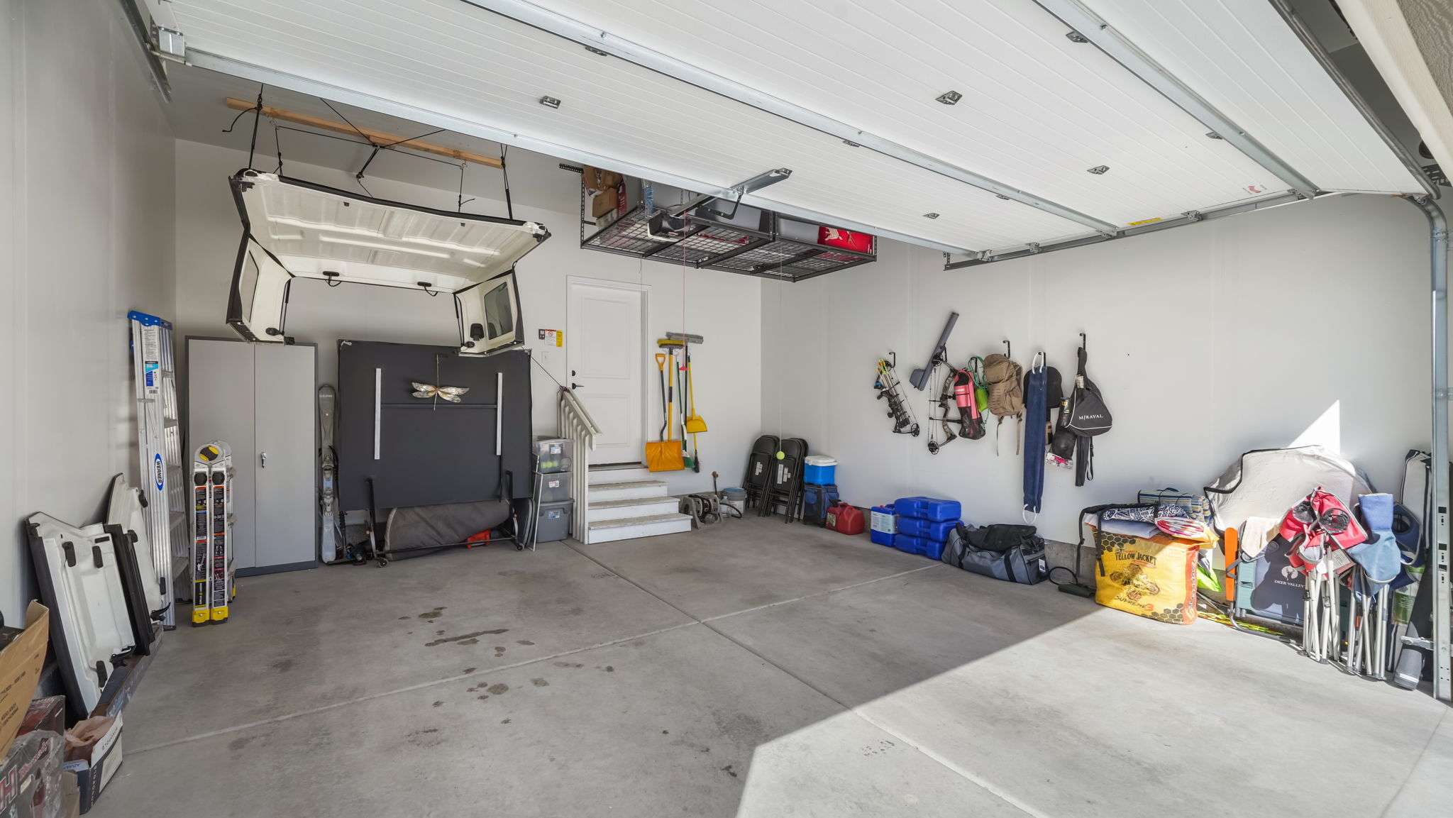 Spacious garage featuring concrete flooring, a white garage door, overhead storage racks, and finished white painted walls