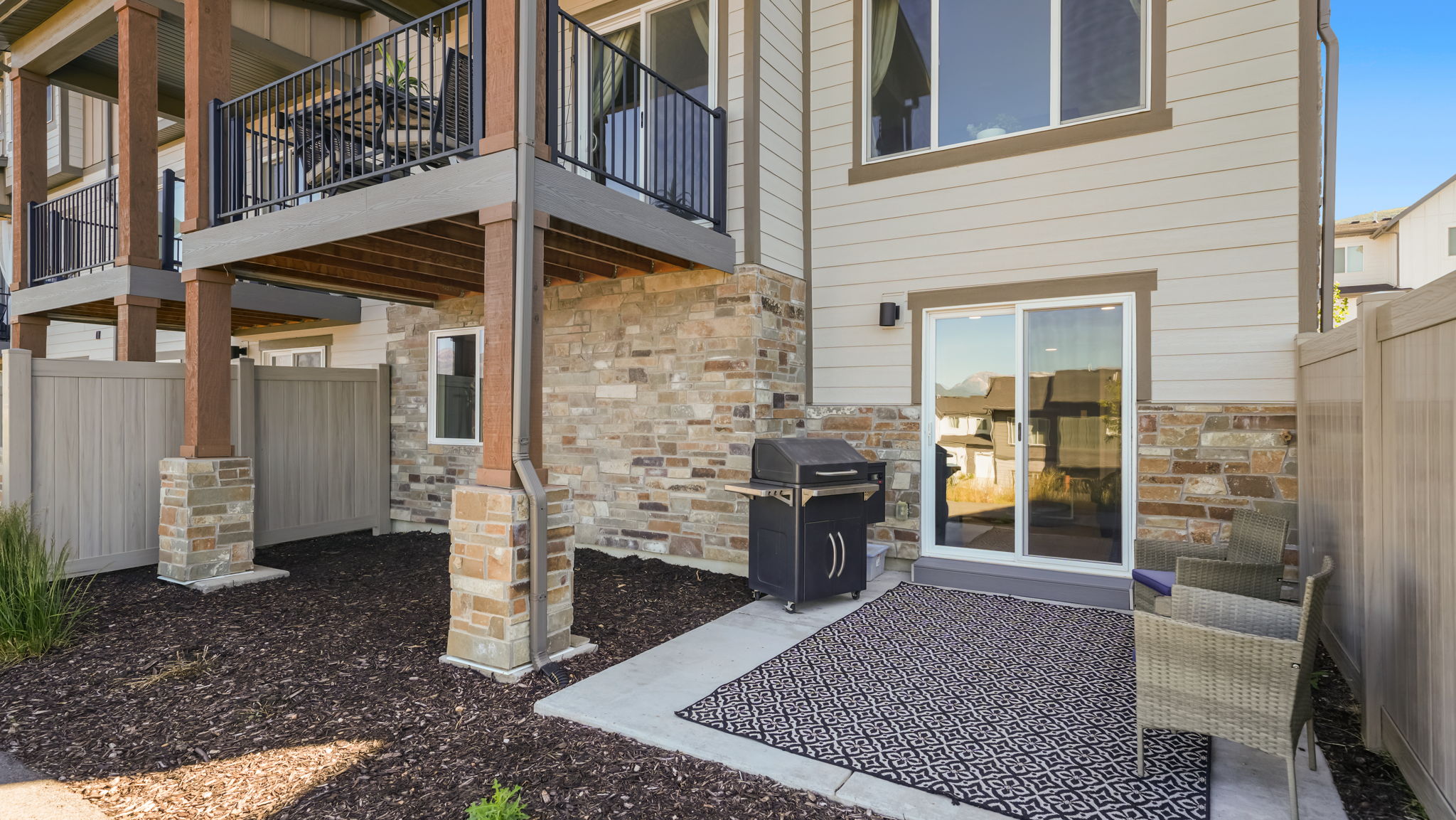 Private patio space featuring a concrete slab, sliding glass door access, and an exterior wall clad in horizontal siding and stone veneer