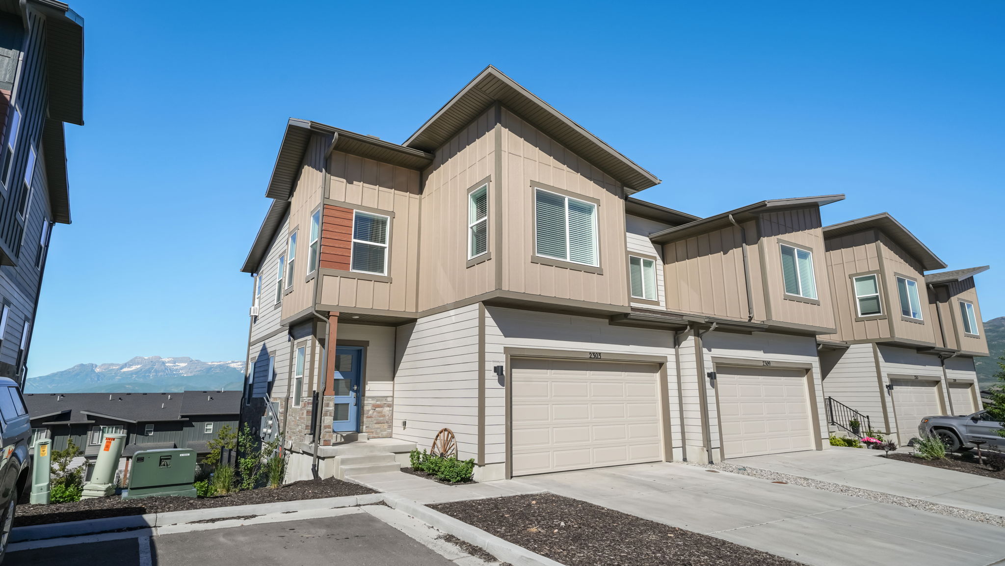 Modern townhouse exterior featuring a two-car garage, multi-toned siding, stone accents, and an entry porch