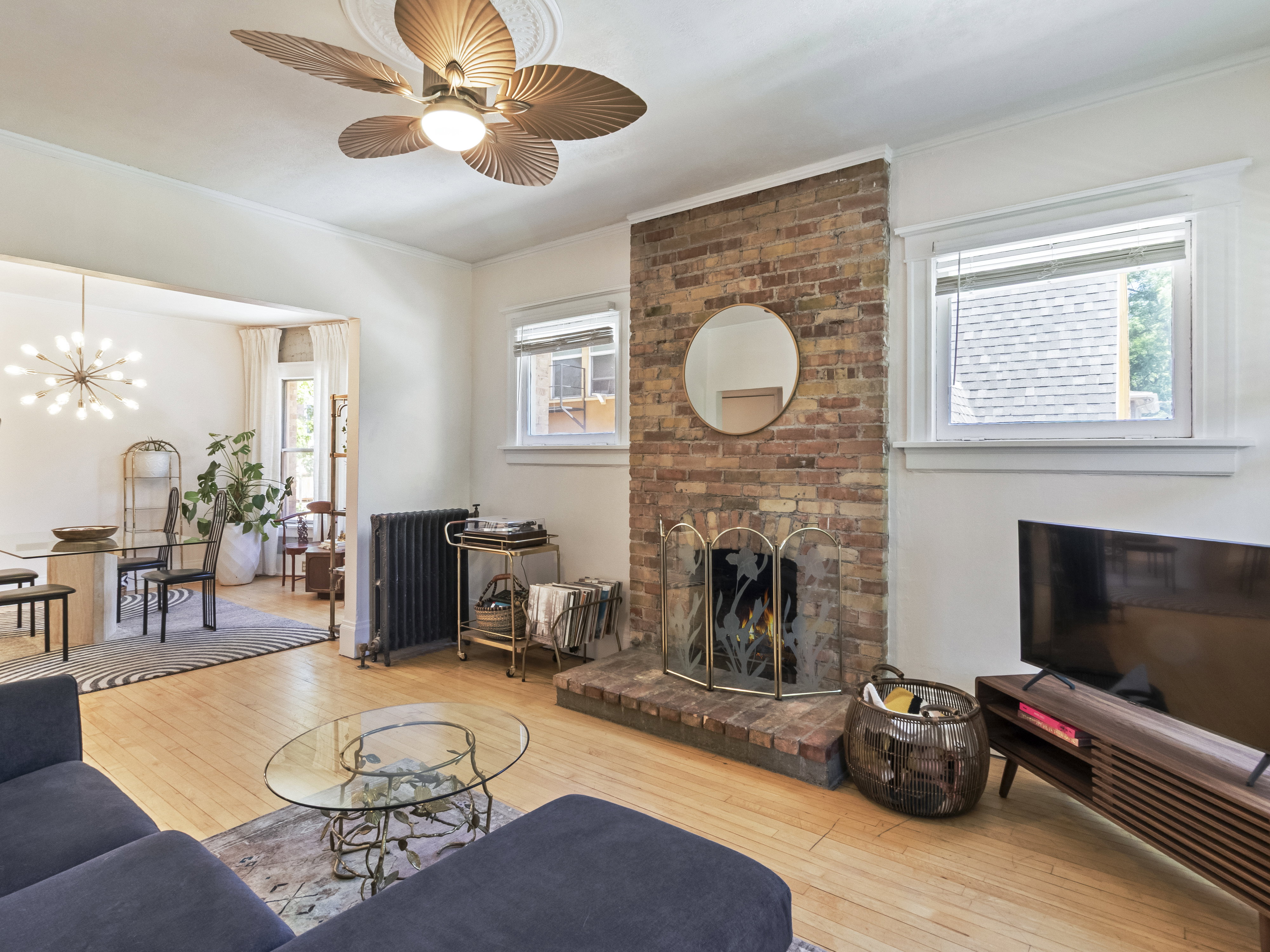 Living area featuring hardwood flooring, a brick fireplace, a decorative ceiling fan, and a radiator