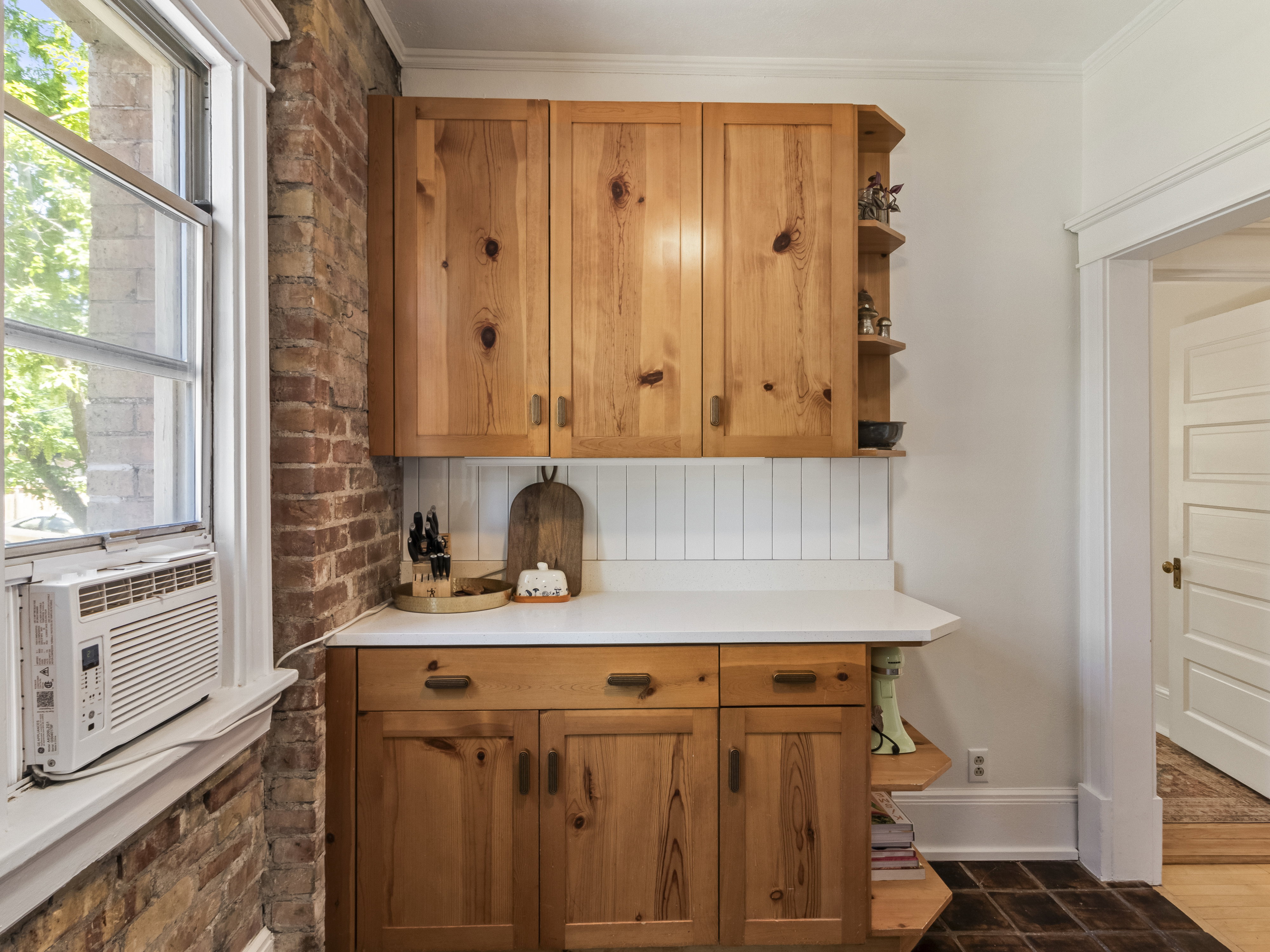Natural wood-finish cabinetry featuring integrated shelving, white countertops, and a white beadboard backsplash