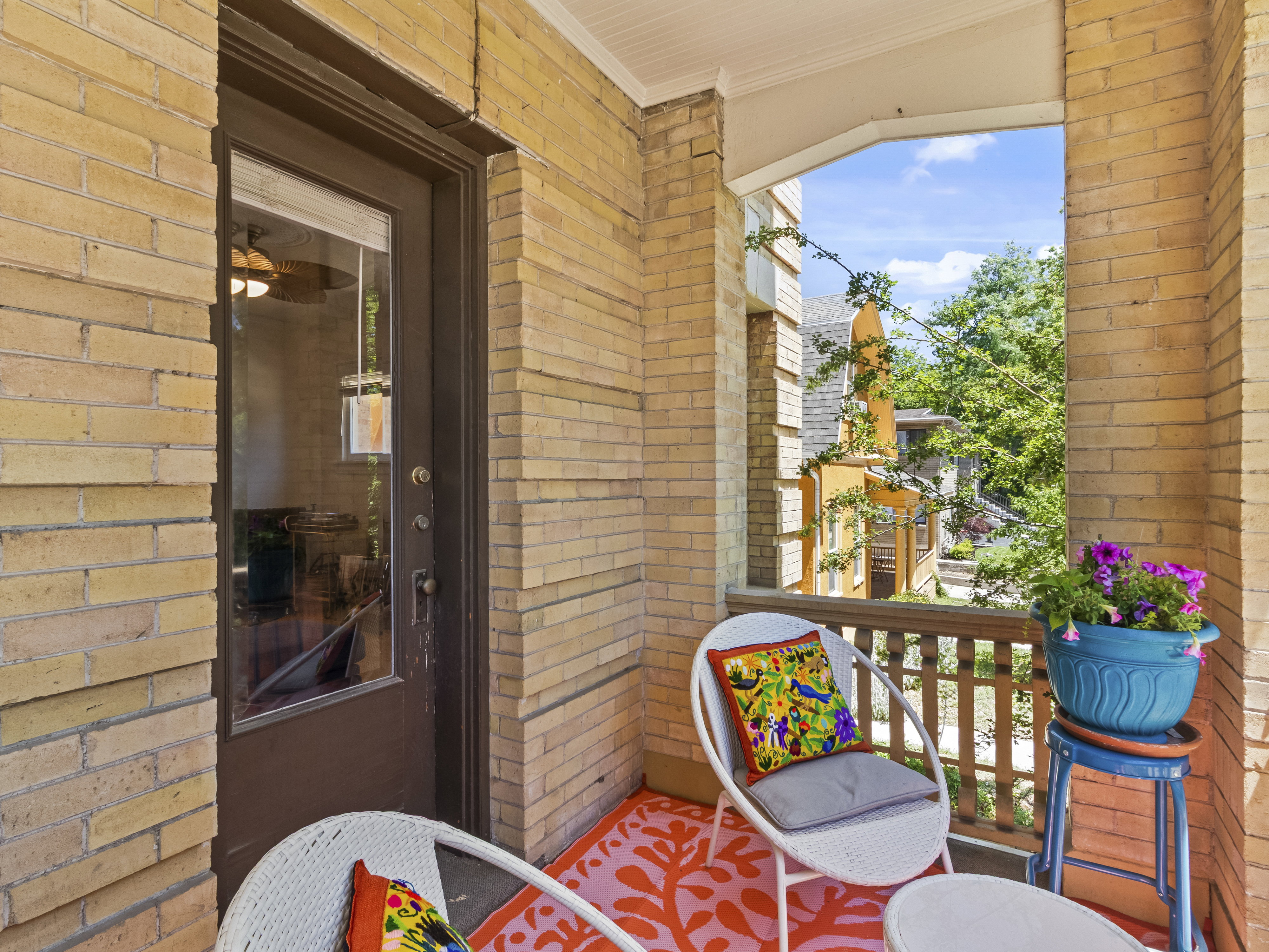 Brick exterior balcony with wooden railing, a glass-paned door, and natural light