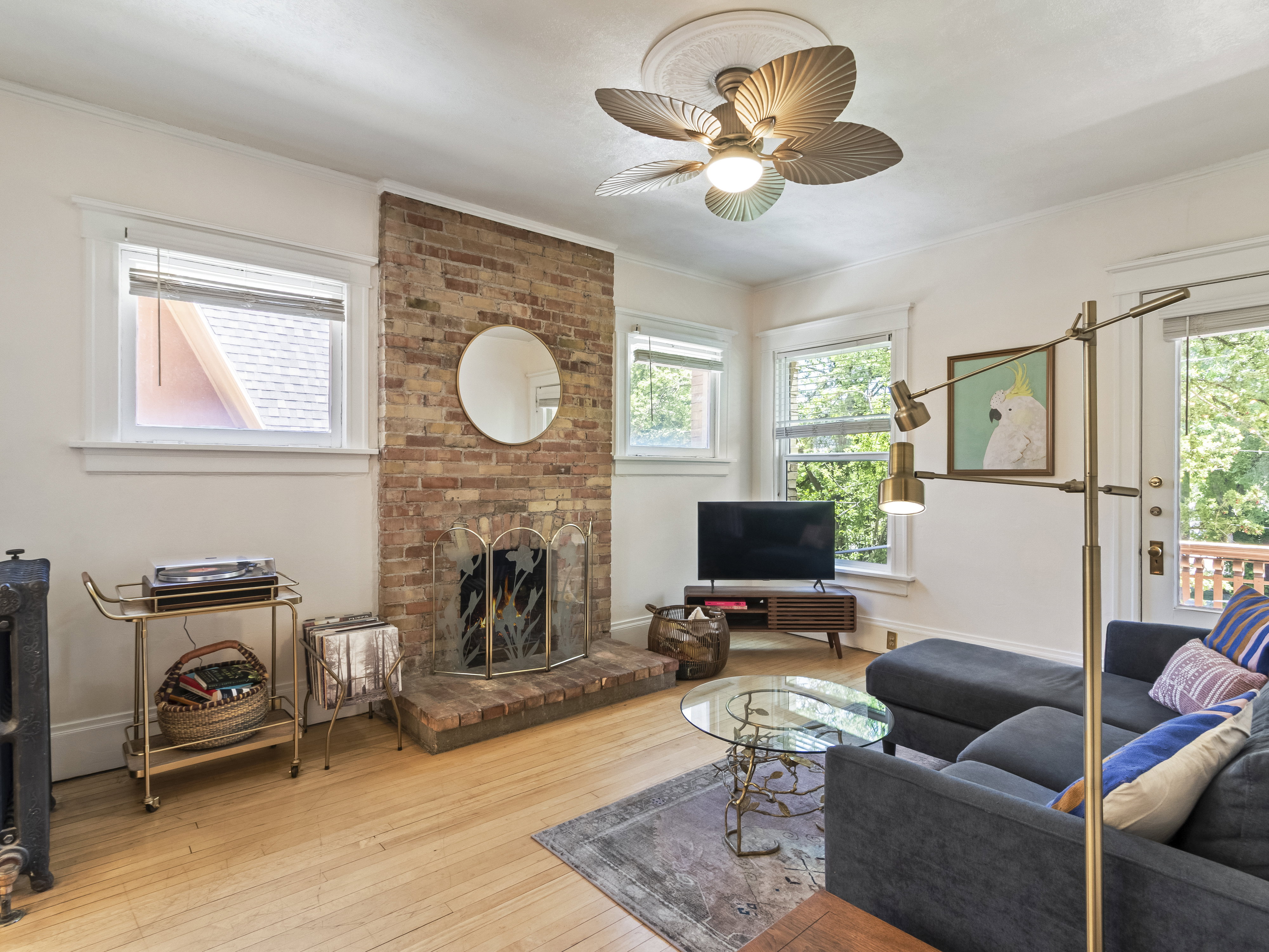 Living area featuring a brick fireplace with a metal screen, light wood-finish flooring, multiple windows, a ceiling fan with a medallion, and a white trim package