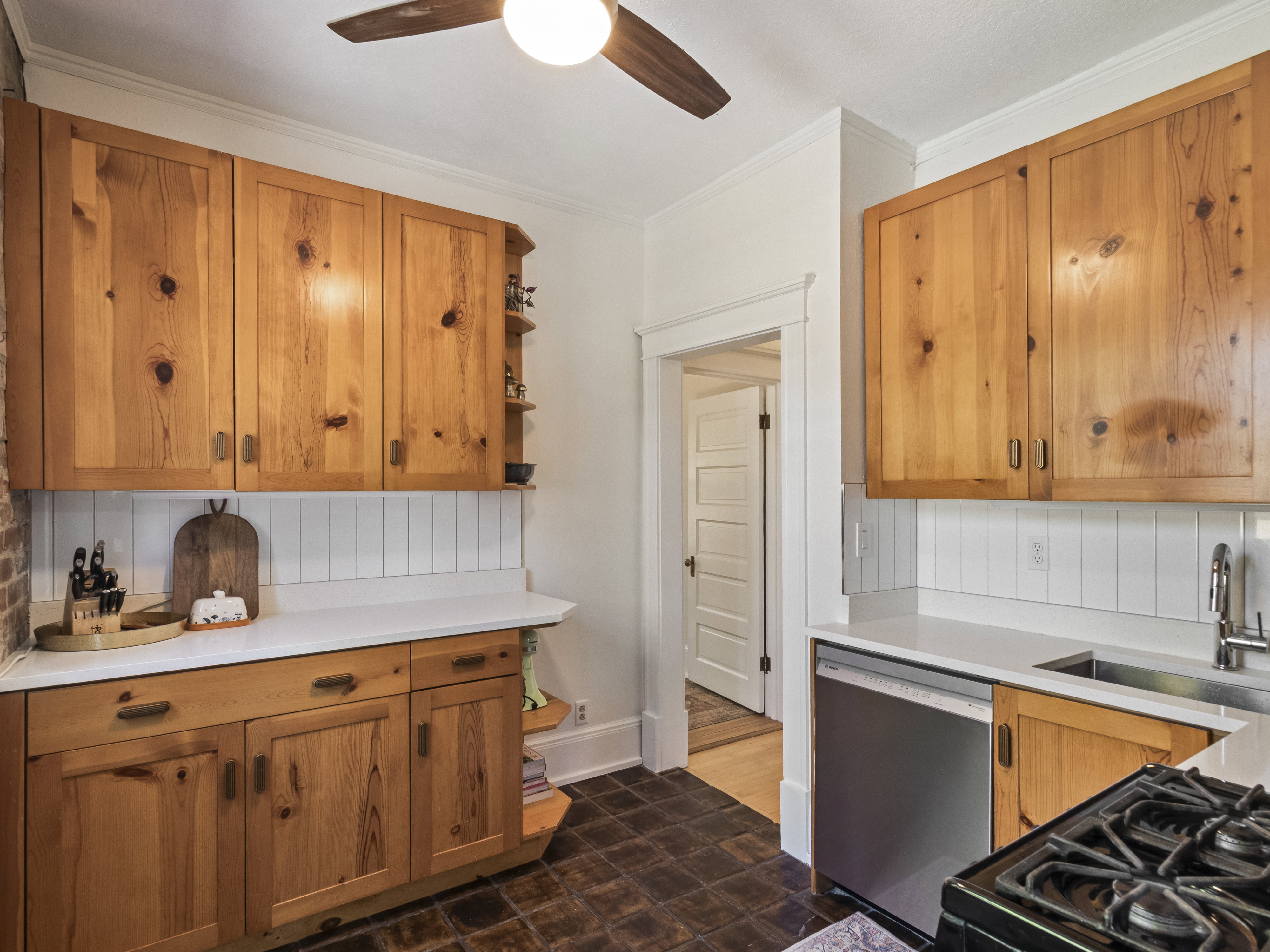 Kitchen featuring natural wood cabinetry, white countertops, white vertical panel backsplash, stainless steel appliances, and dark tile flooring