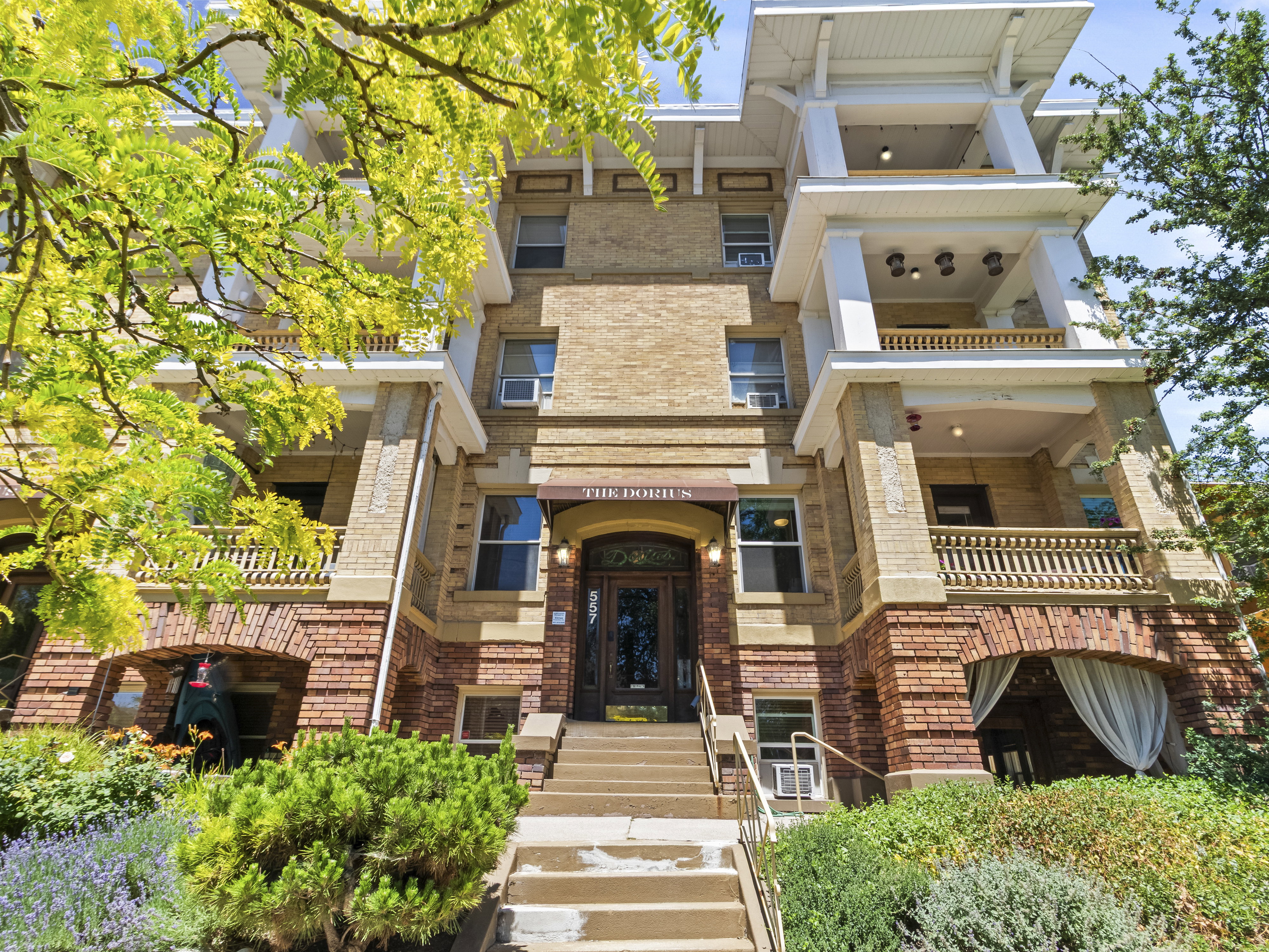 Four-story brick building facade featuring stone accents, balconies with decorative railings, and a prominent arched entryway