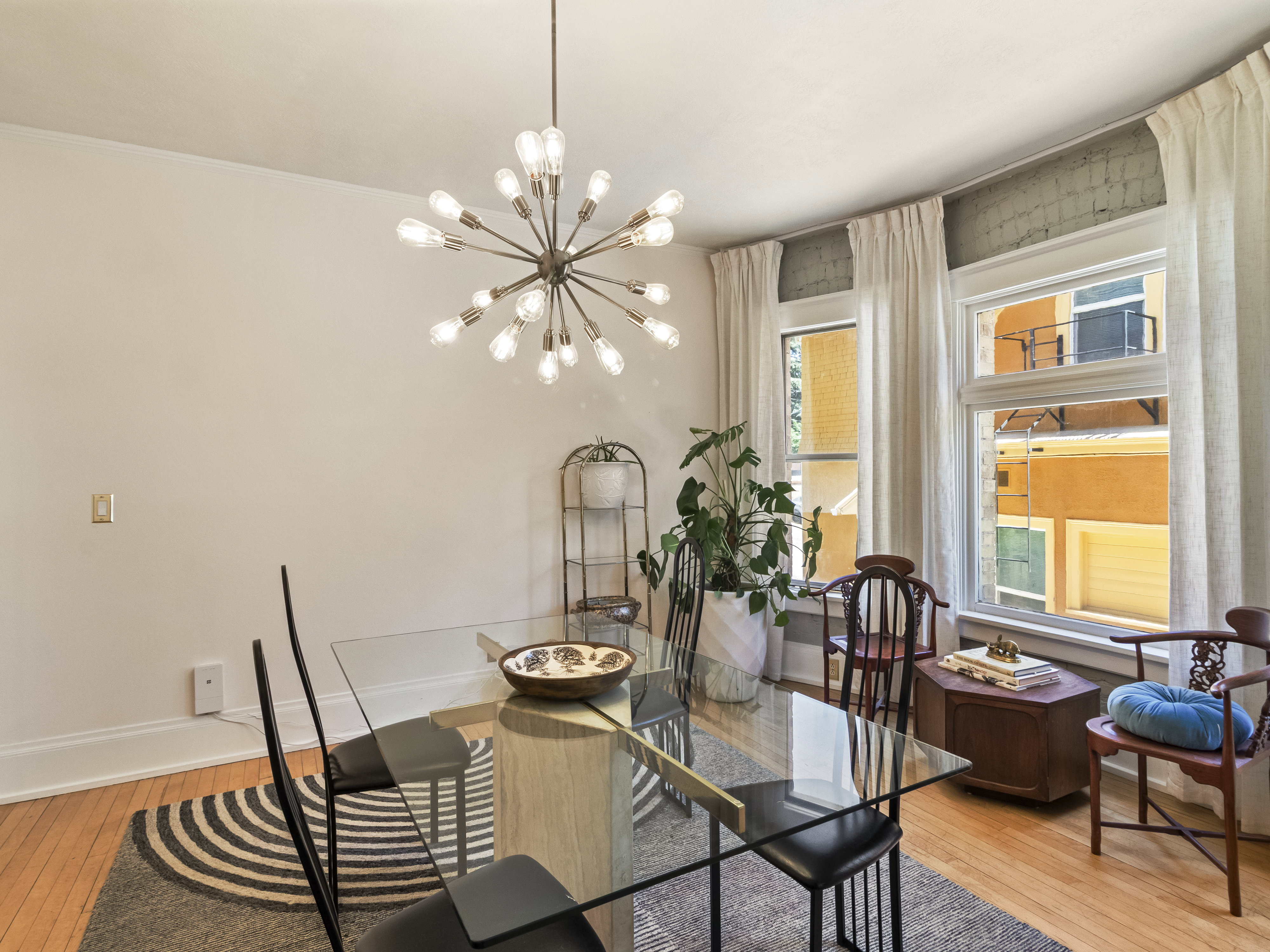 Dining area featuring a contemporary sputnik chandelier, light hardwood flooring, and multiple windows with white drapery