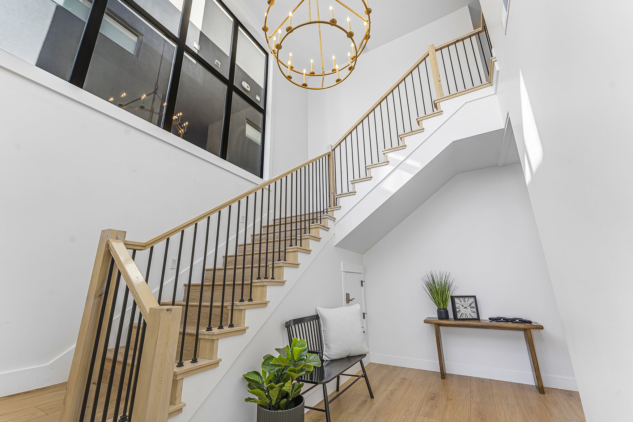 Two-story entry featuring a grand staircase with natural wood treads and handrails, black metal balusters, a large gold-finish chandelier, and a prominent upper window with black framing
