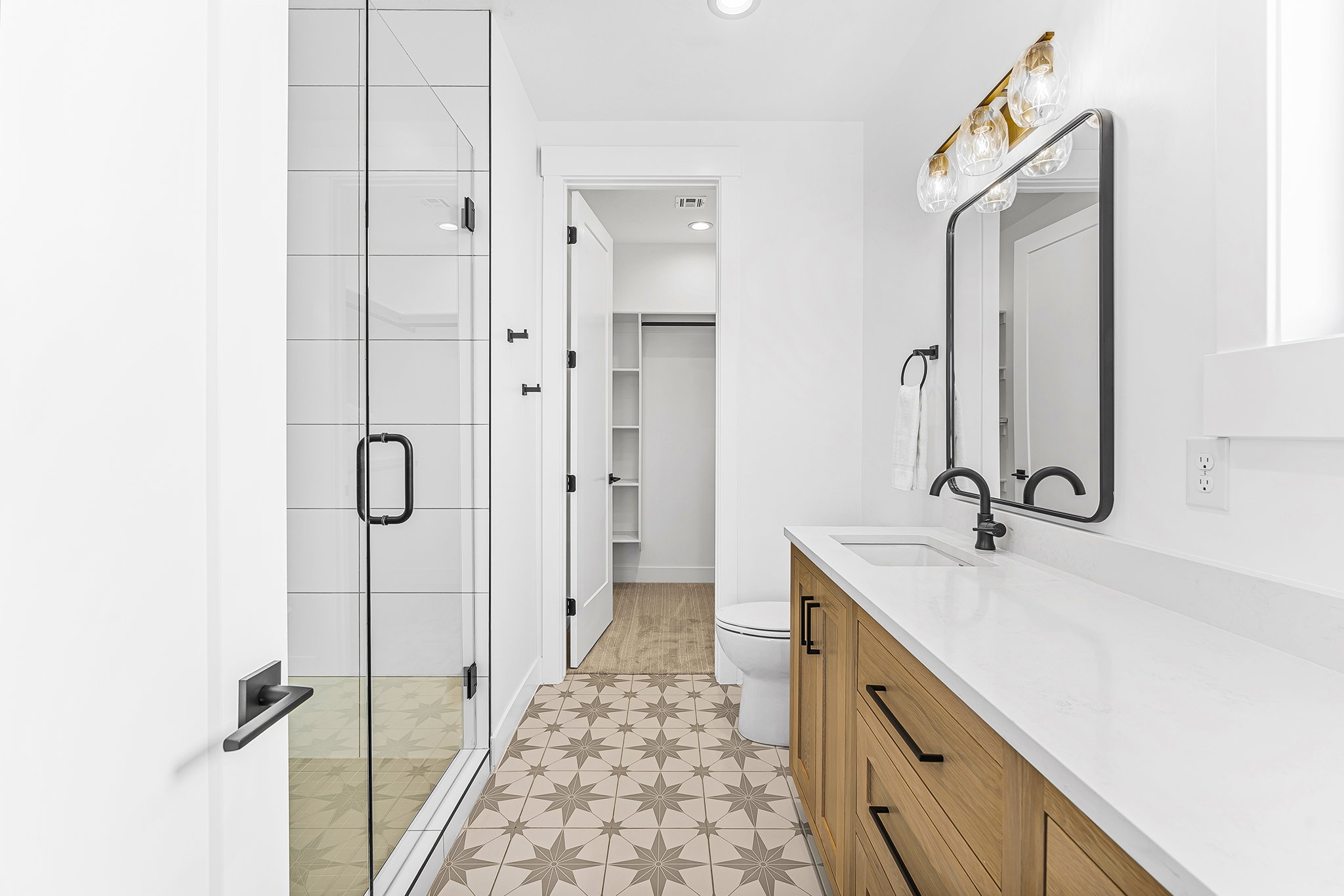 Bathroom featuring a glass-enclosed shower, patterned floor tile, wood-finish vanity with ample storage, white countertop, and contemporary lighting fixture