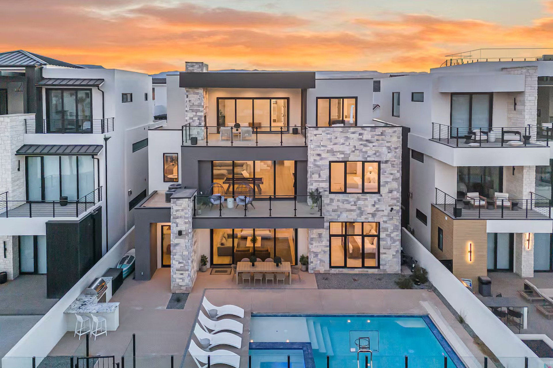 Multi-level contemporary residence featuring extensive balconies with glass railings, a private swimming pool, outdoor kitchen with built-in grill, and stone facade accents