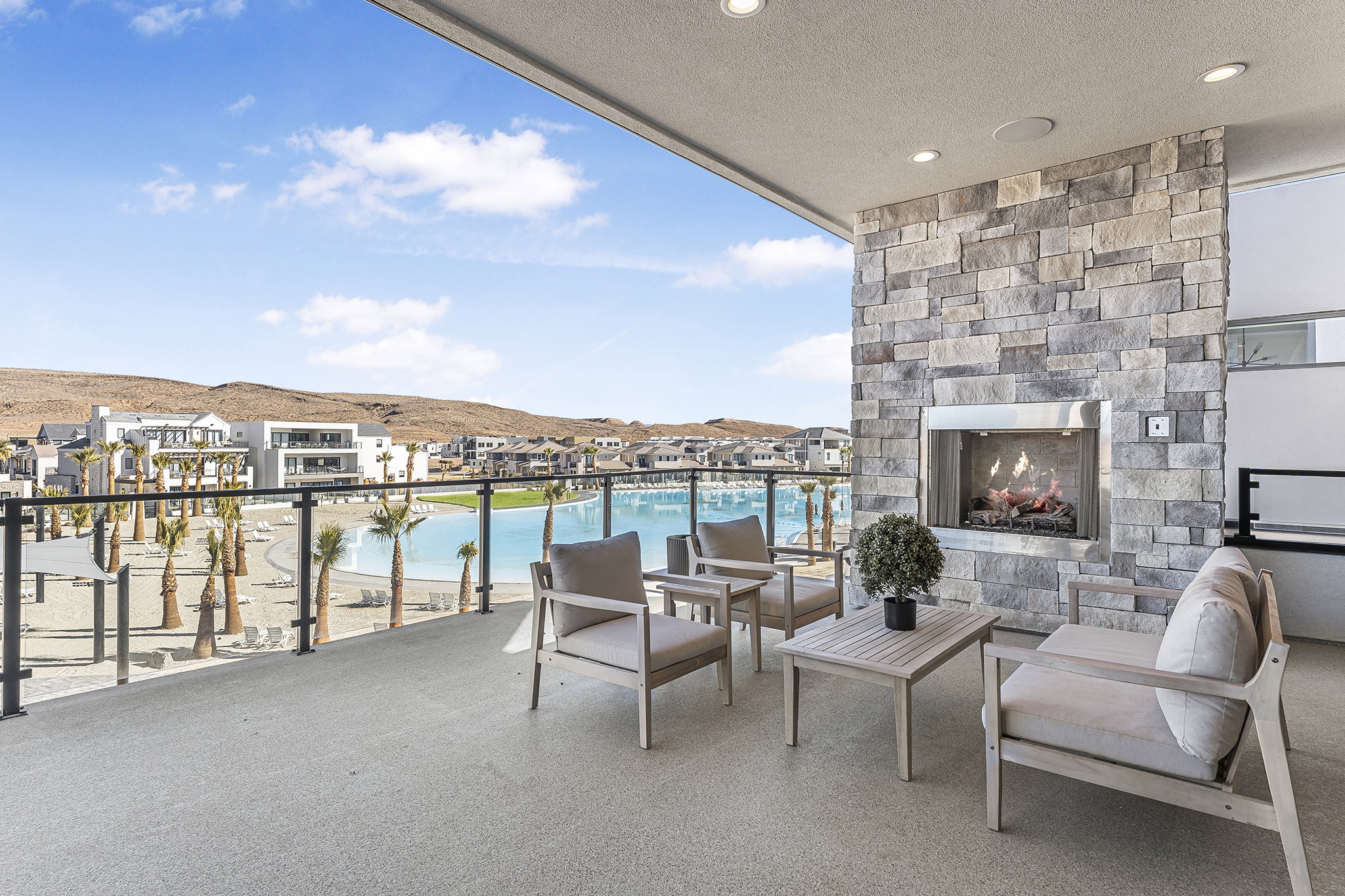 Expansive outdoor terrace featuring a stone-clad fireplace with a stainless steel insert, recessed lighting, and a glass-paneled railing