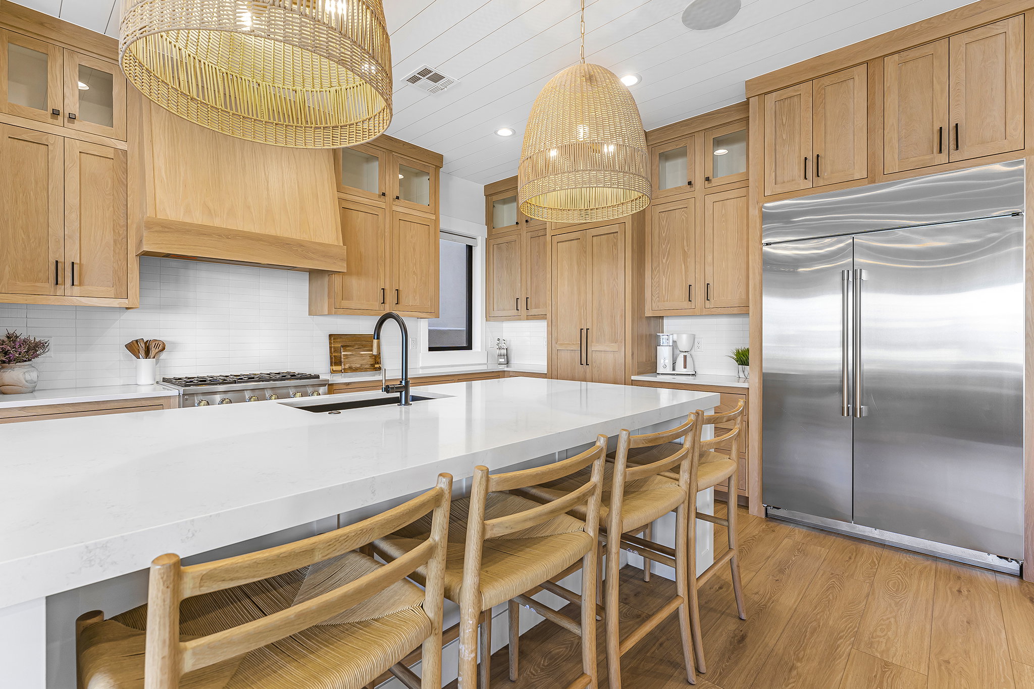 Spacious kitchen featuring a large central island with seating, natural wood cabinetry, stainless steel appliances, white subway tile backsplash, and wood-finish flooring