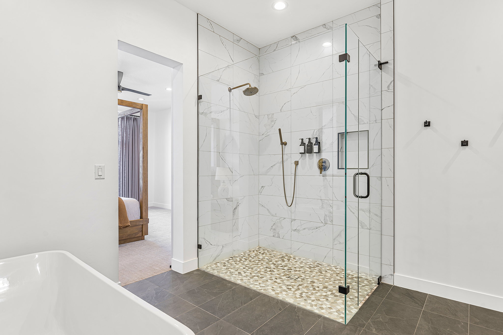 Spacious walk-in shower featuring a glass enclosure, white marble-look tile, and a pebble-stone floor