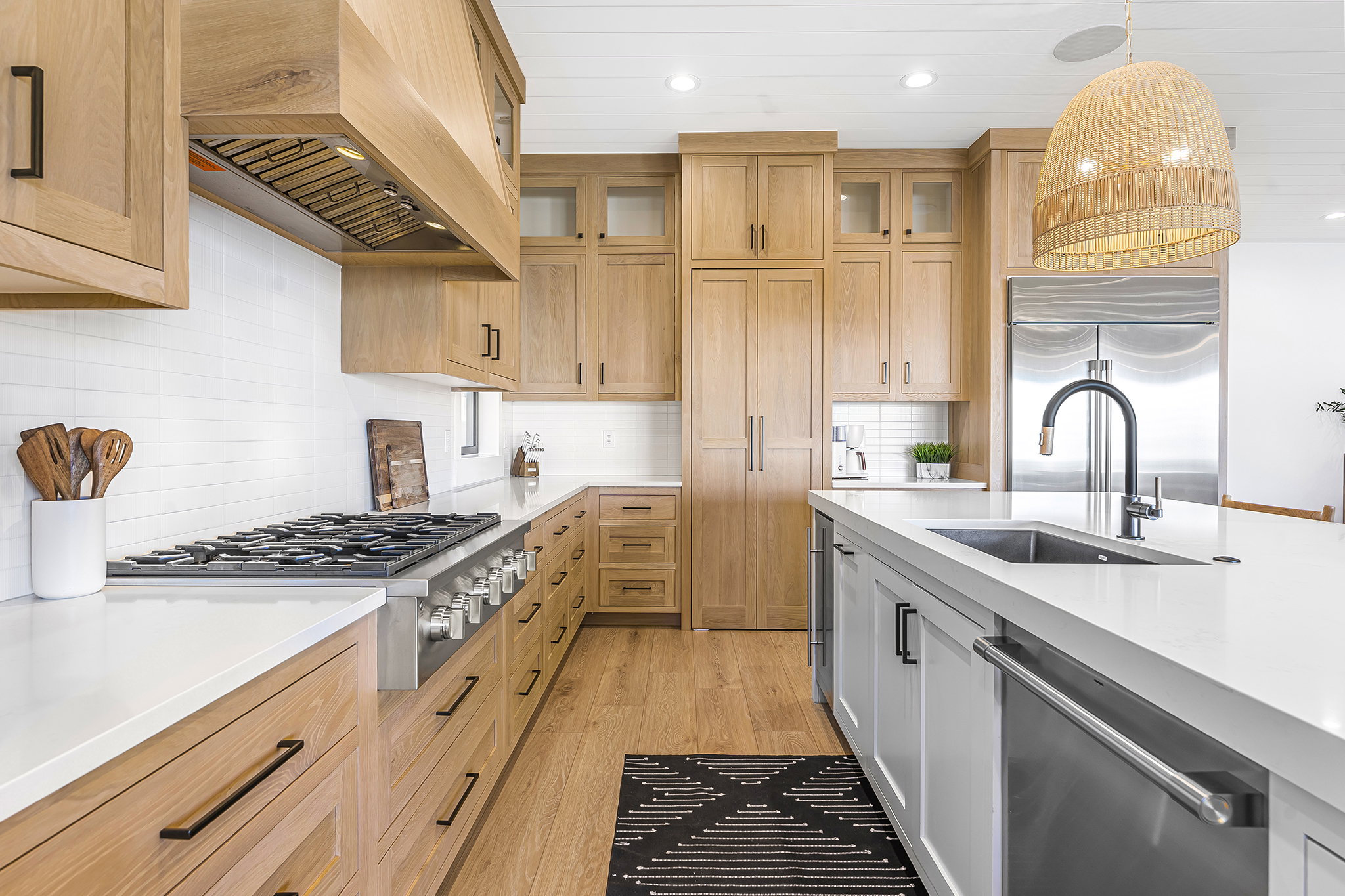 Gourmet kitchen featuring natural wood cabinetry, professional-grade range, stainless steel appliances, a center island with sink, and white countertops