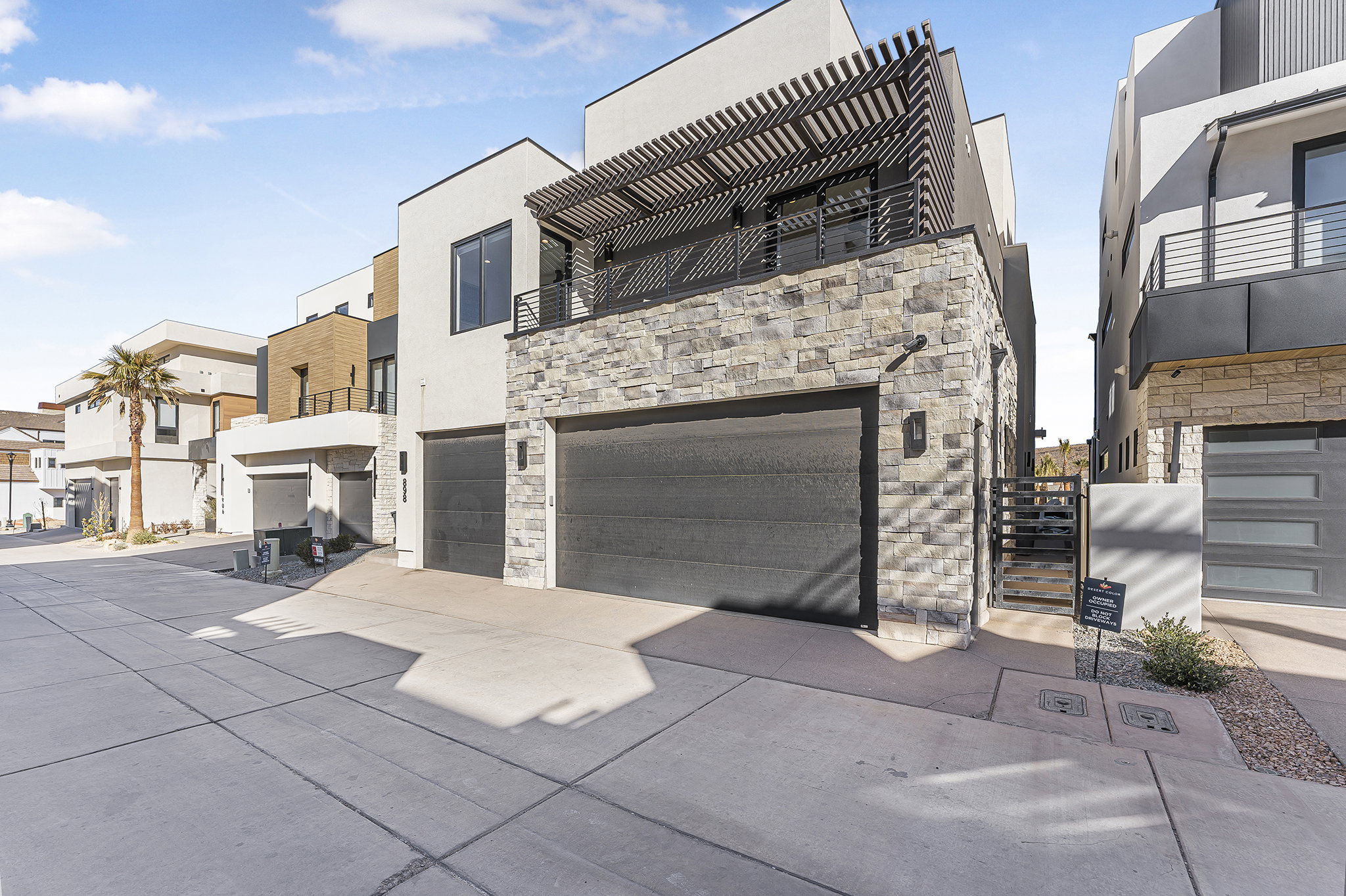Modern-style exterior featuring a stone facade, two-car garage, and a second-story balcony with a slatted pergola