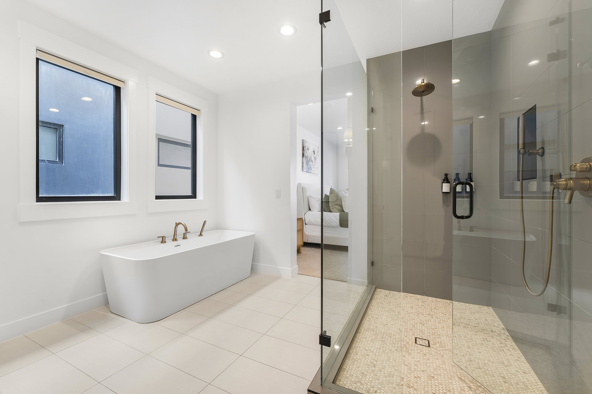 Freestanding soaking tub with floor-mounted brass fixtures, set against a backdrop of two black-framed windows