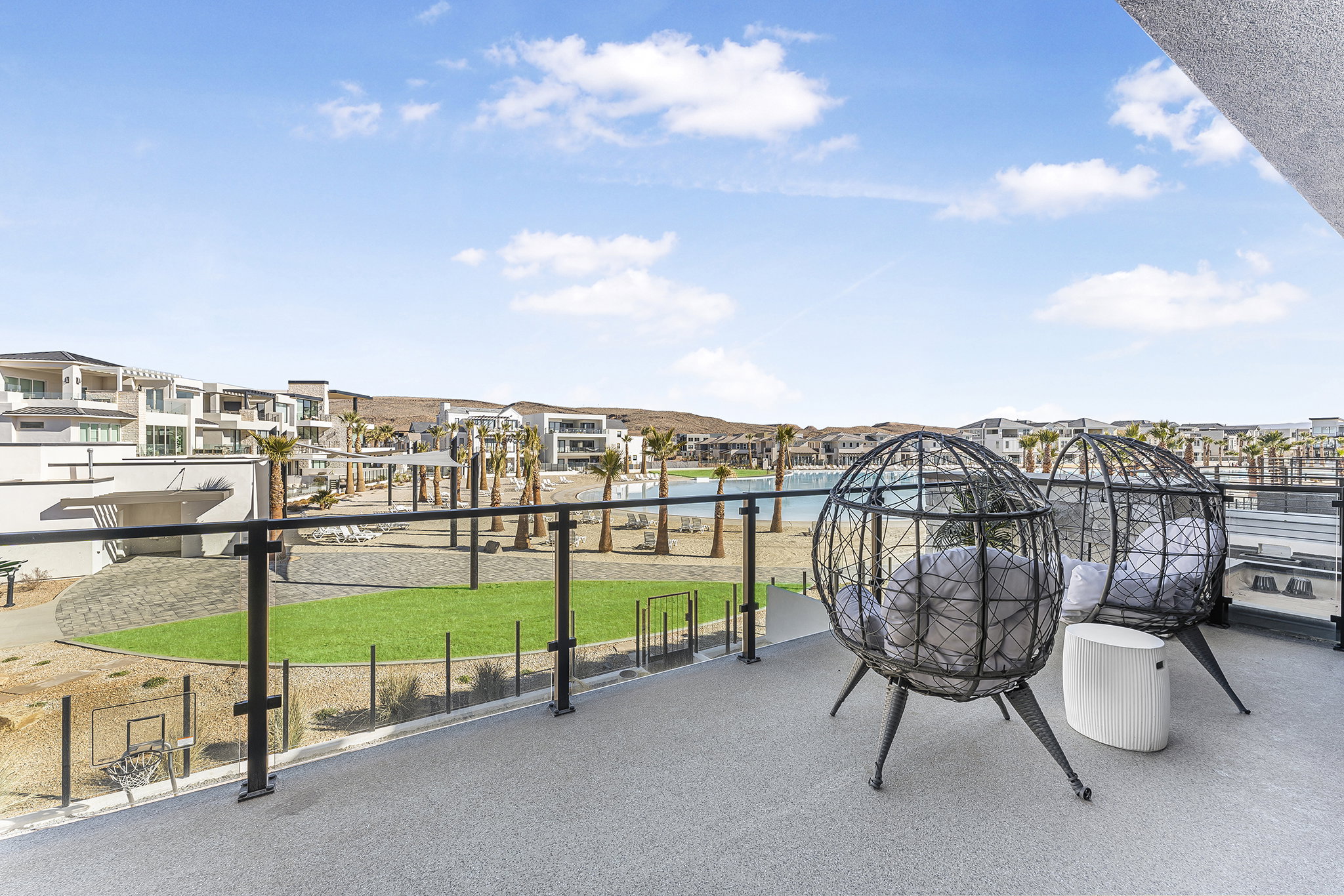 Private balcony with glass railing system overlooking a landscaped common area, water feature, and contemporary architecture