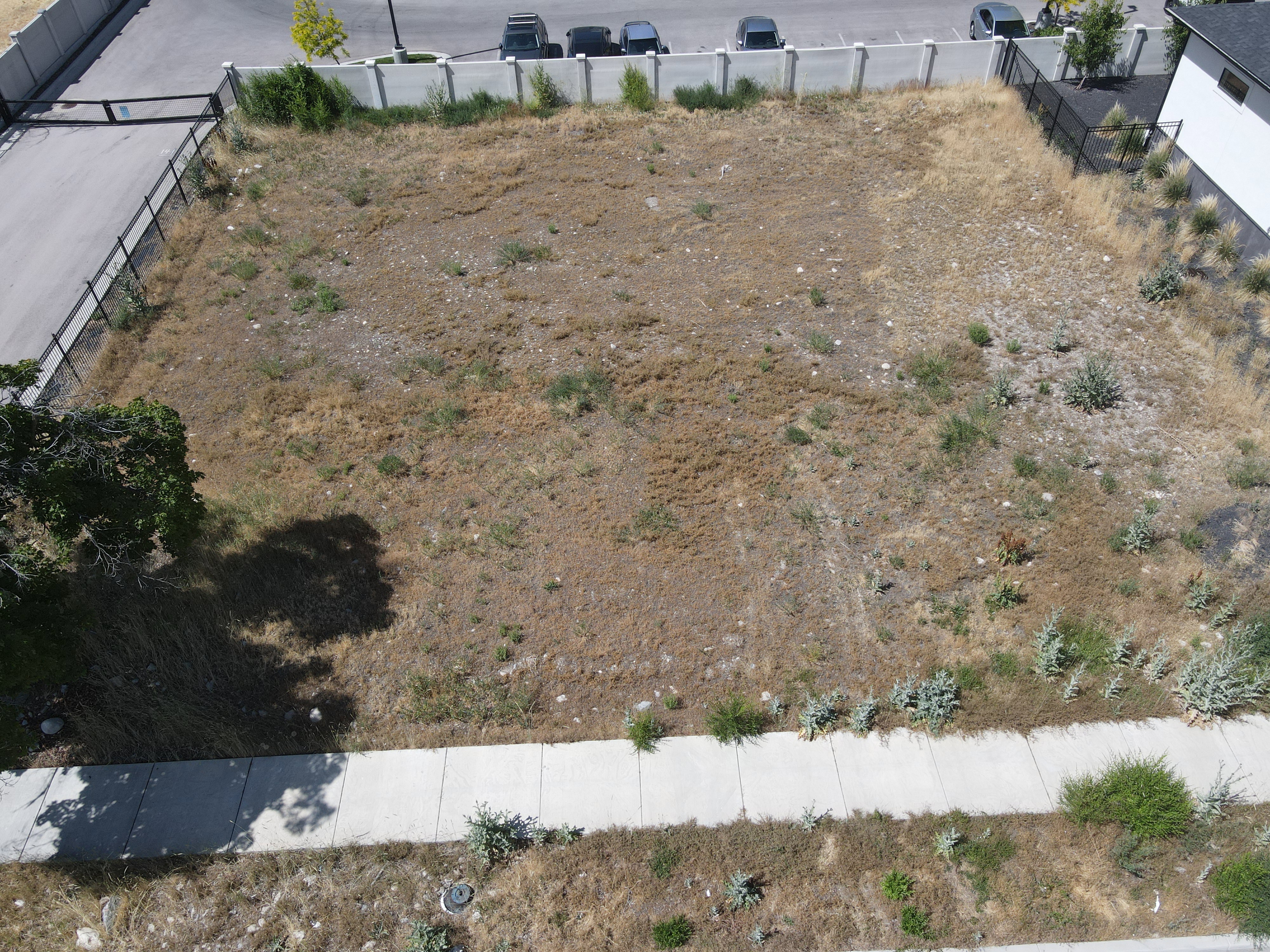 Expansive vacant lot featuring perimeter fencing, an established sidewalk, and street access