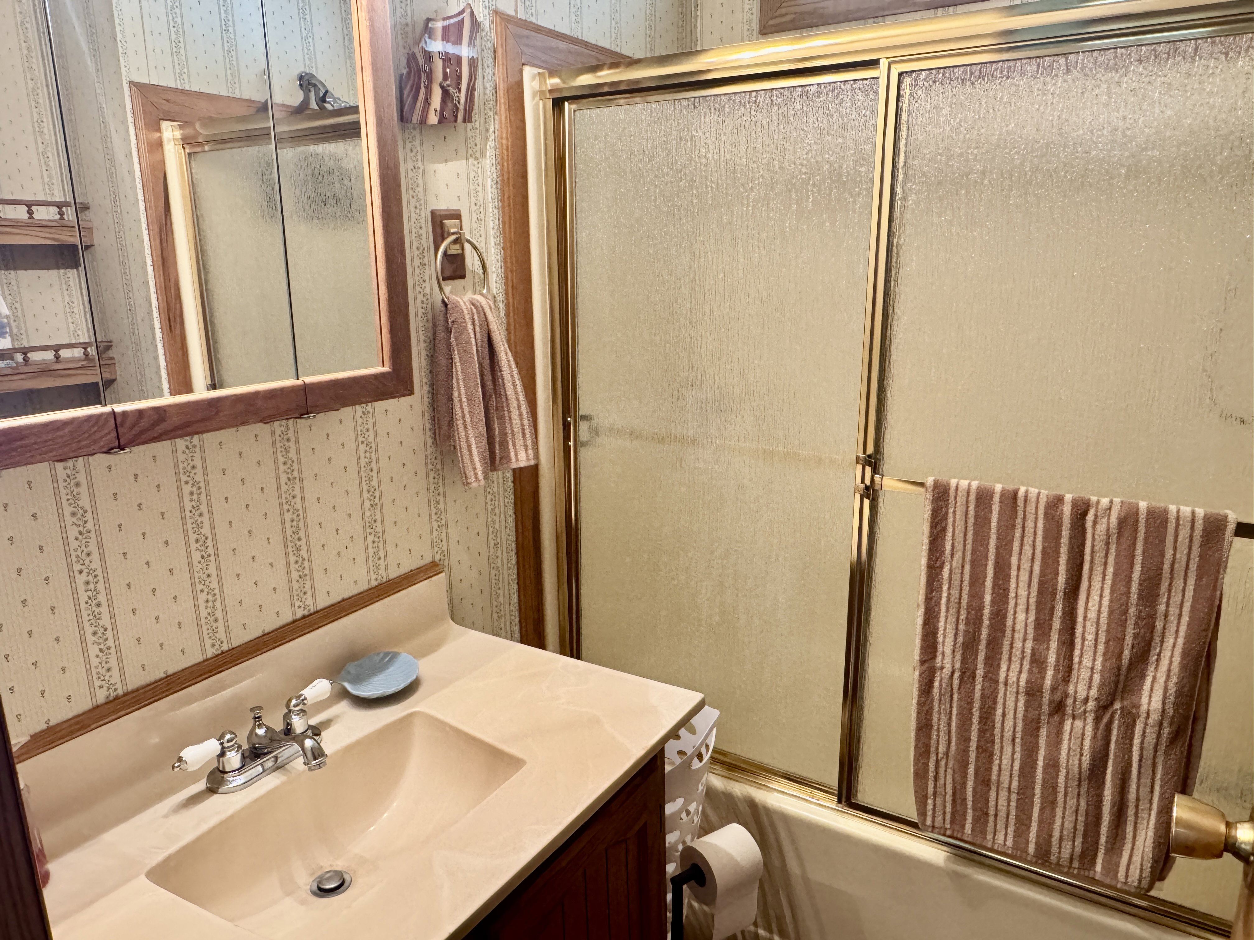 Bathroom featuring a vanity with an integrated sink, polished chrome faucet, wood-finish medicine cabinet, and a bathtub with a framed glass enclosure
