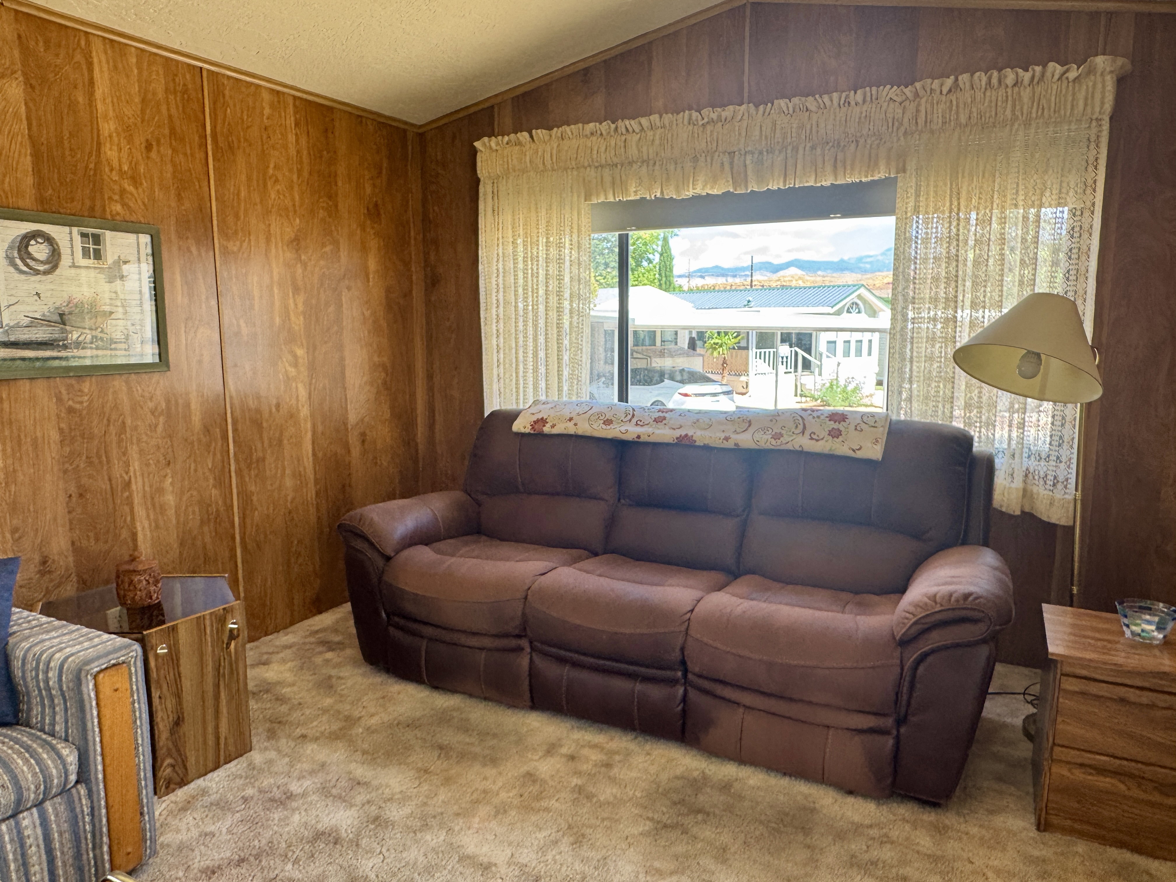 Carpeted interior space featuring wood-panel walls, a large window, and a sloped ceiling