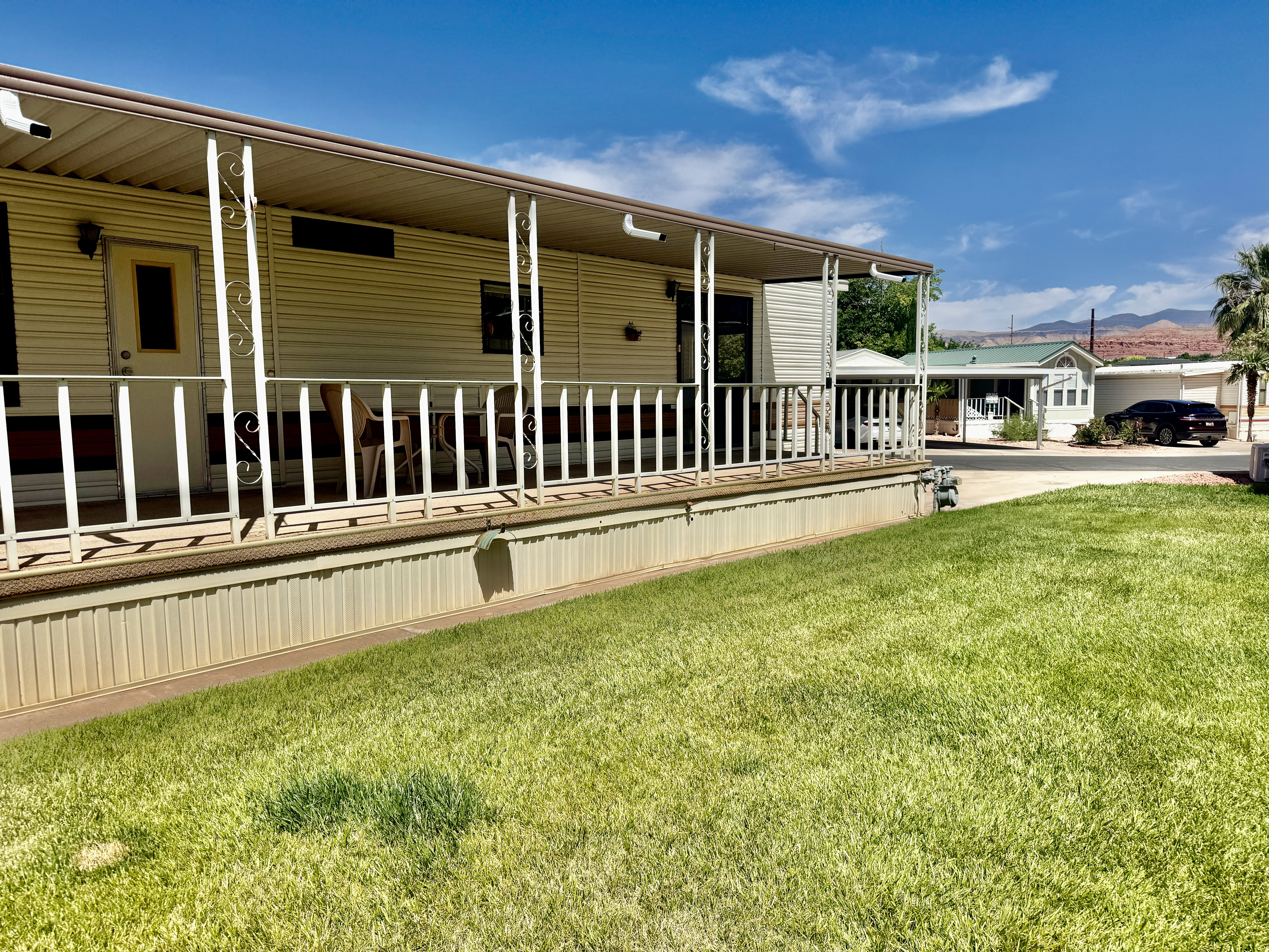 Residential exterior featuring a covered porch with white railing, light-colored siding, and a manicured lawn
