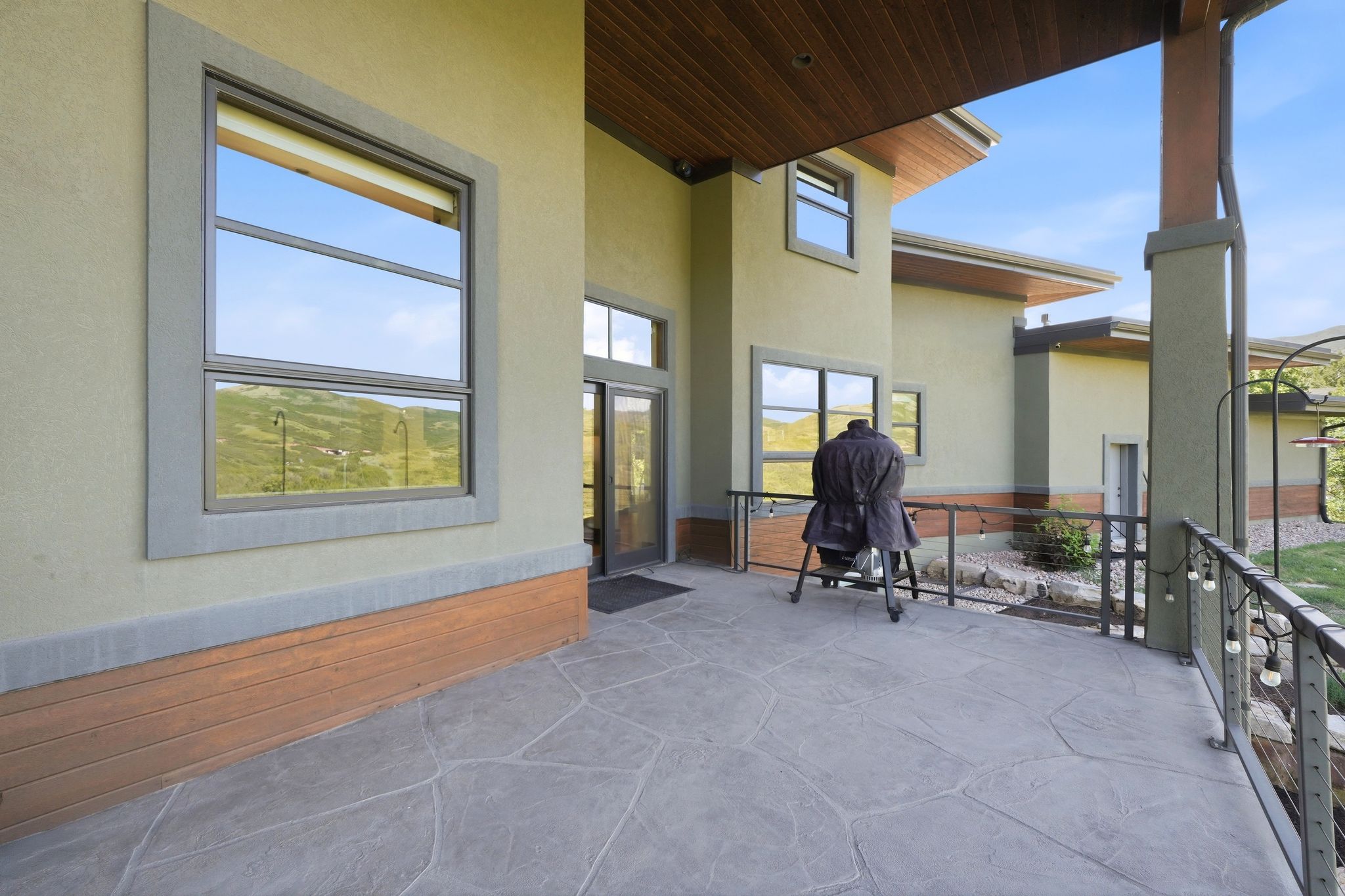 Expansive stamped concrete patio featuring a decorative metal railing, wood-paneled ceiling, and stucco exterior