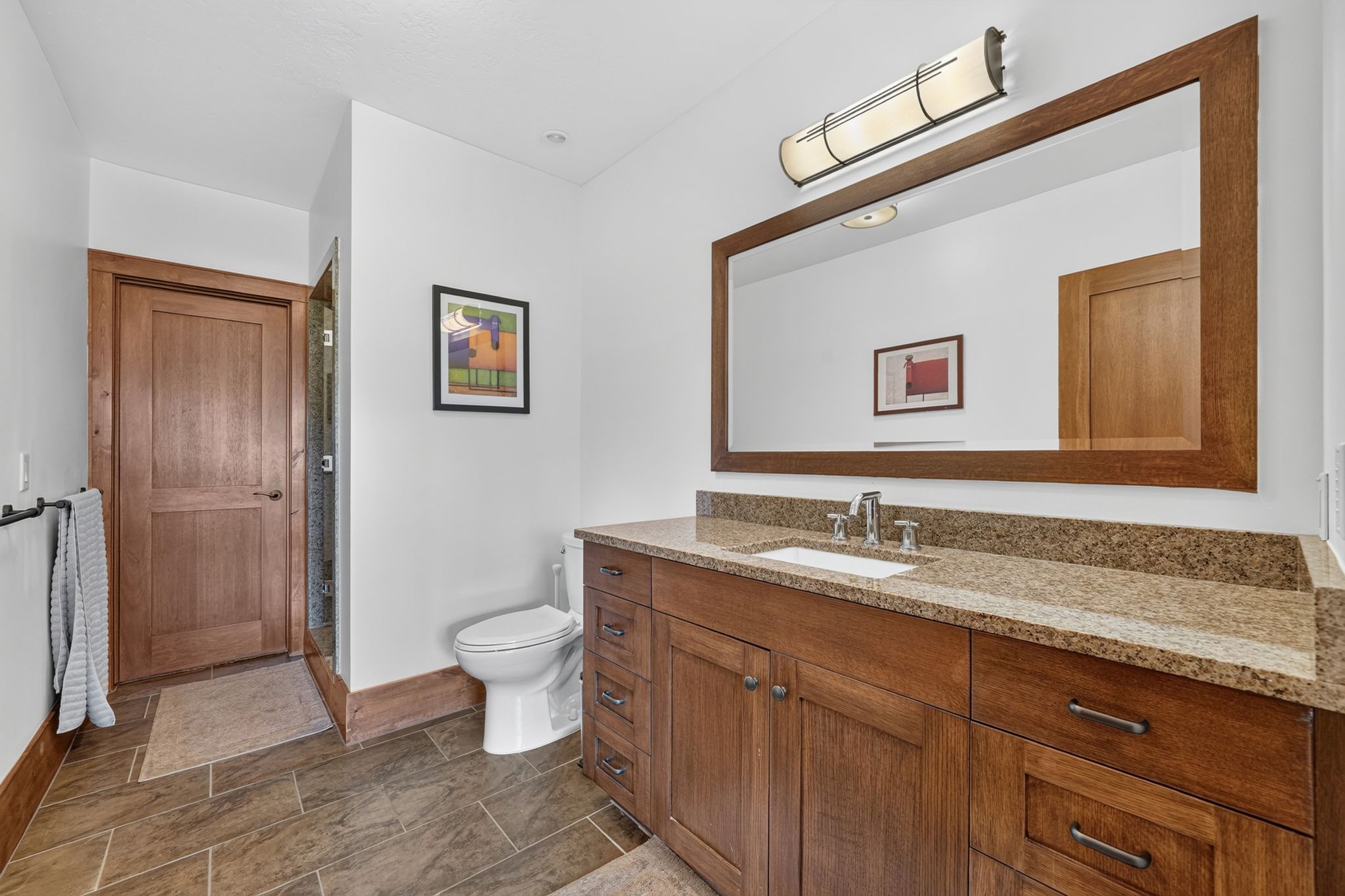 Bathroom featuring a wood-finish vanity with a light granite countertop, an undermount sink, and a large framed mirror