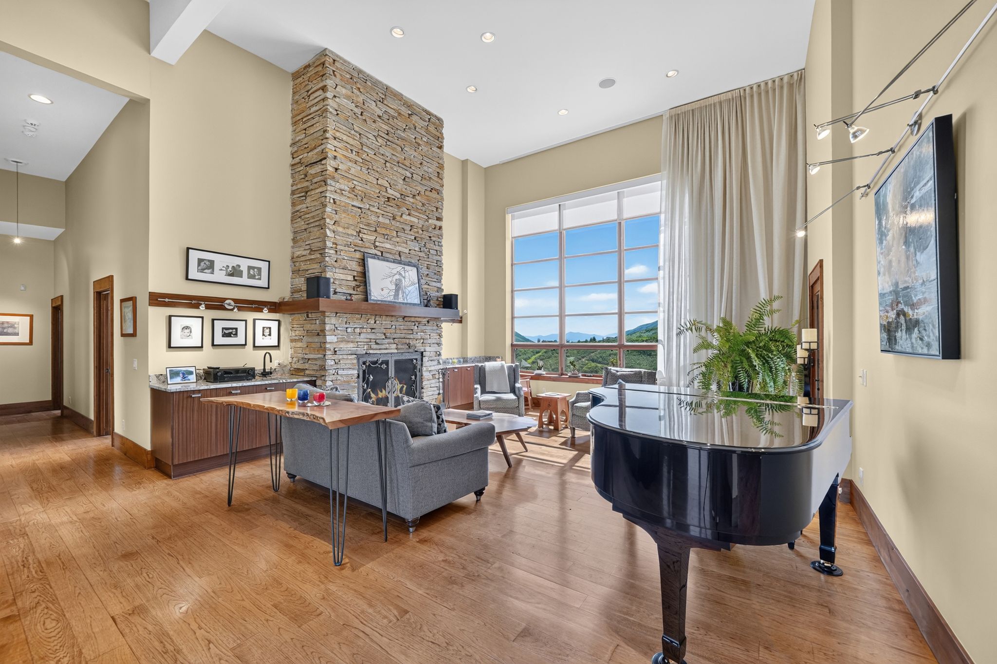 Great room featuring a floor-to-ceiling stone fireplace, high ceilings, wood-finish flooring, a built-in wet bar with a stone countertop, and expansive window wall