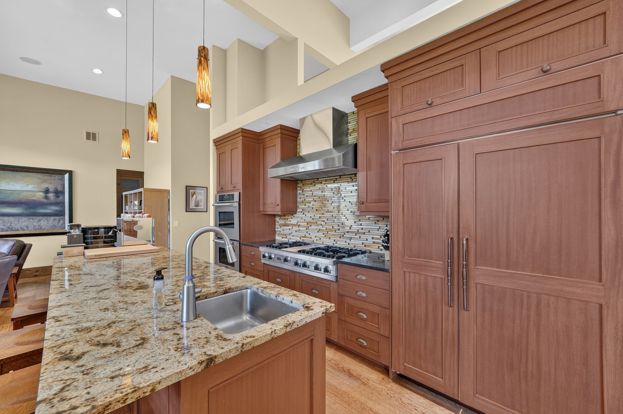 Gourmet kitchen featuring a large island with an undermount sink, granite countertops, wood-finish cabinetry, a stainless steel range with matching hood, and built-in panel-ready refrigeration