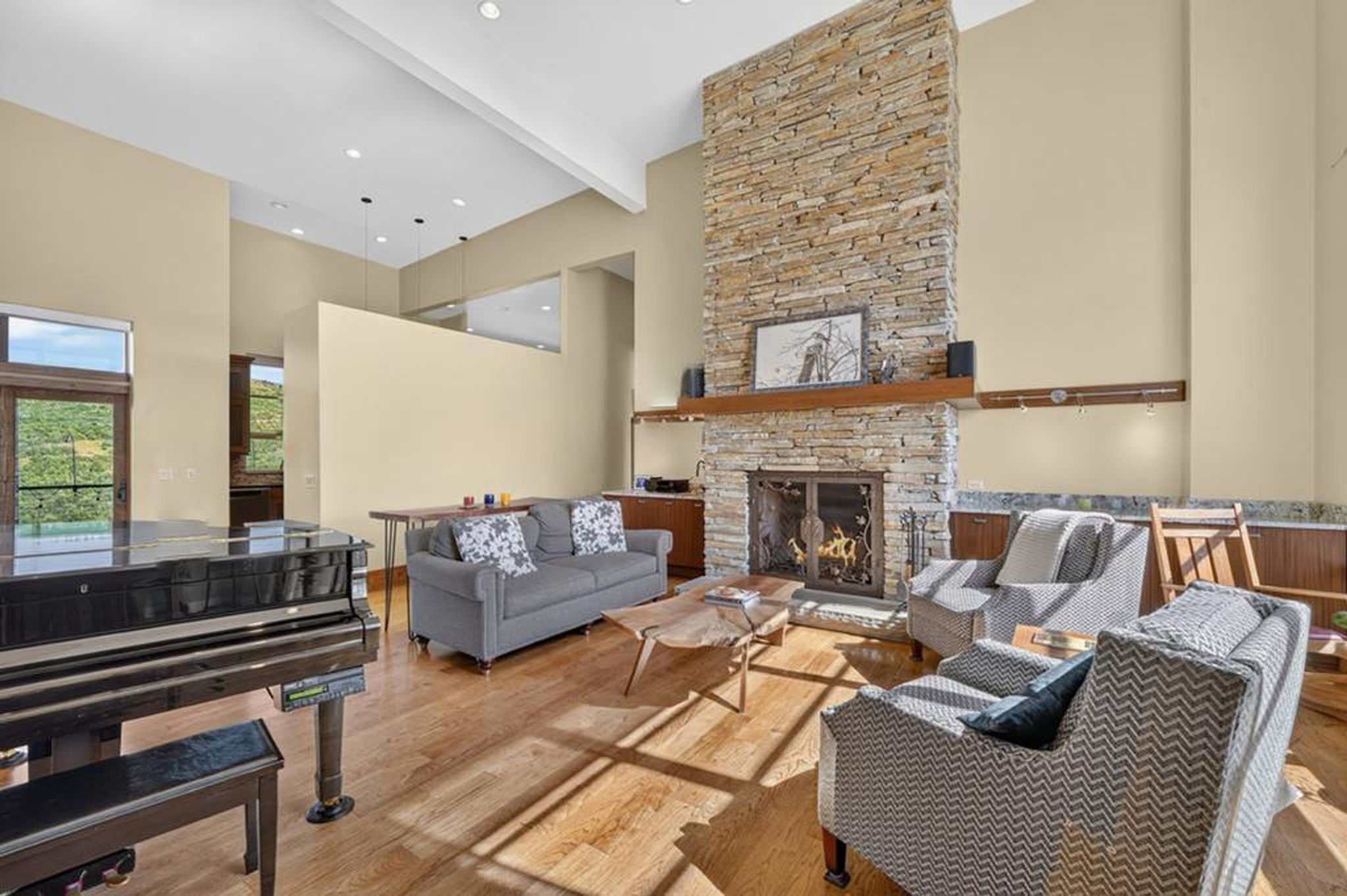 Spacious living area featuring a floor-to-ceiling stone fireplace, vaulted ceilings, wood-finish flooring, and a large glass door opening to outdoor scenery