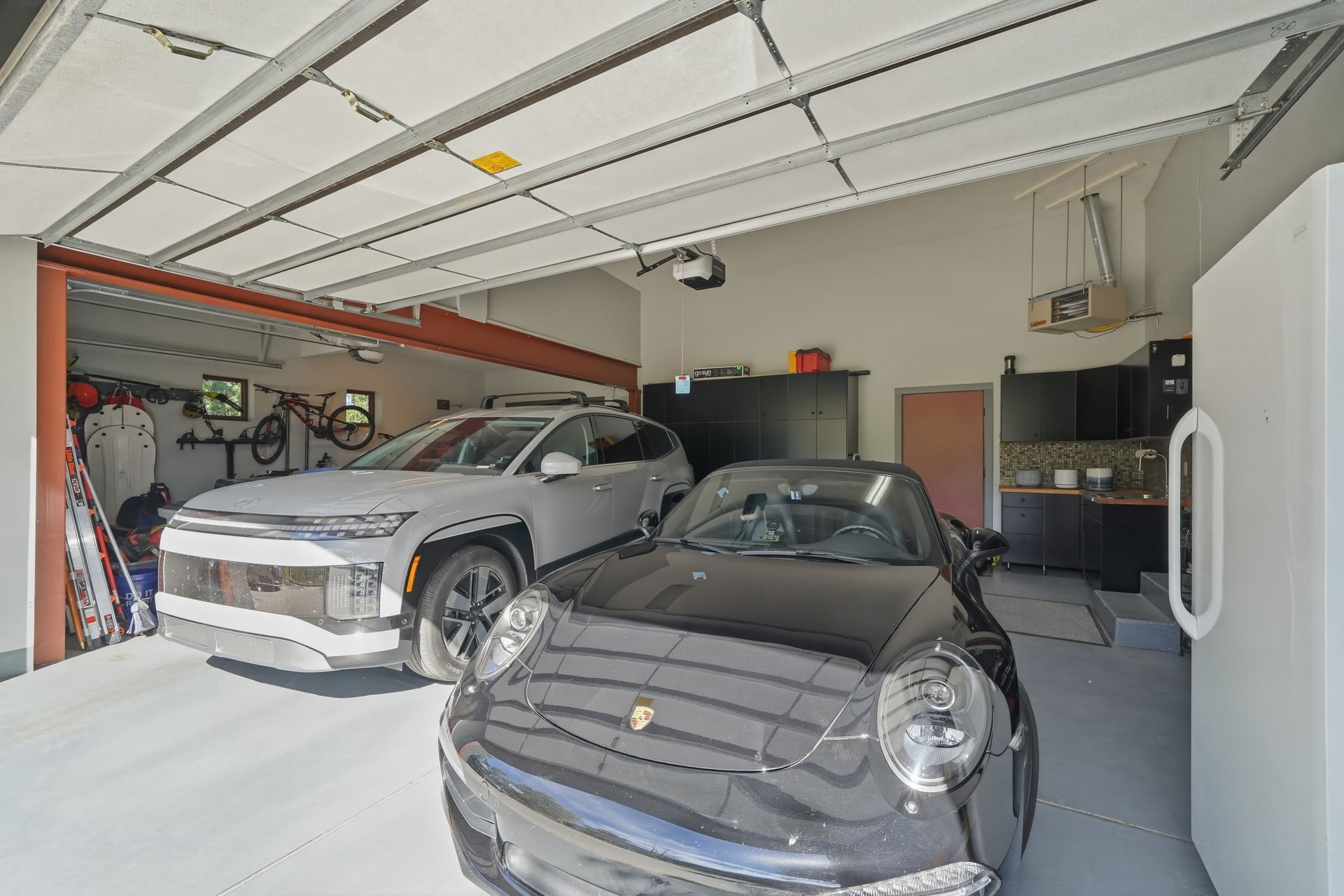 Spacious garage featuring two vehicle bays, a utility sink with mosaic tile backsplash, built-in black cabinetry, and a concrete floor