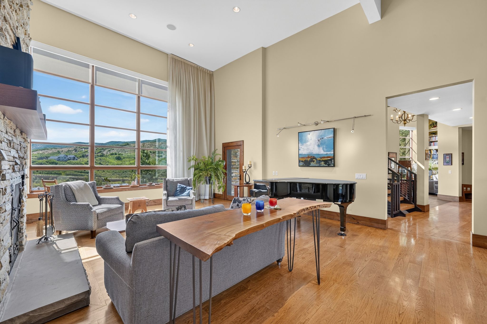 Living space featuring a prominent stone-clad fireplace with a stone hearth, high ceilings, large multi-pane windows with mountain scenery, and light wood-finish flooring