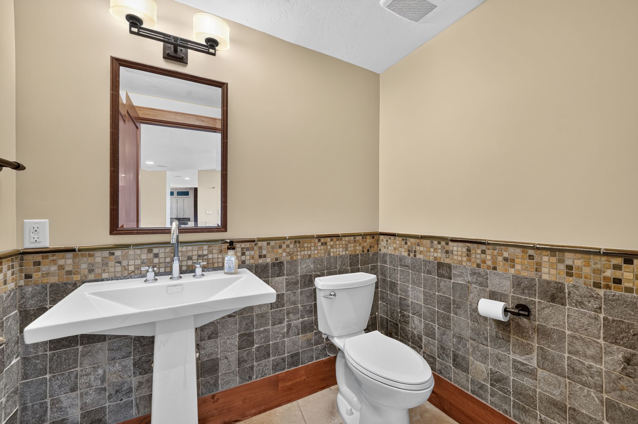 Pedestal sink with chrome faucet, framed mirror, and dual vanity light fixture