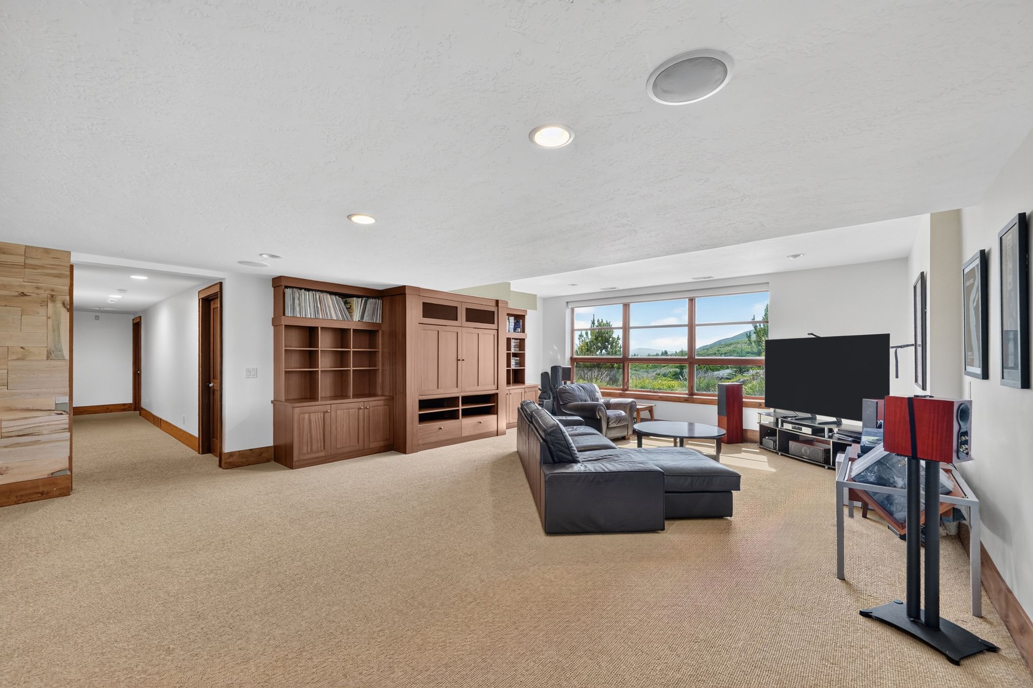 Spacious entertainment room featuring broad windows with exterior scenery, built-in cabinetry, recessed lighting, and integrated ceiling speakers