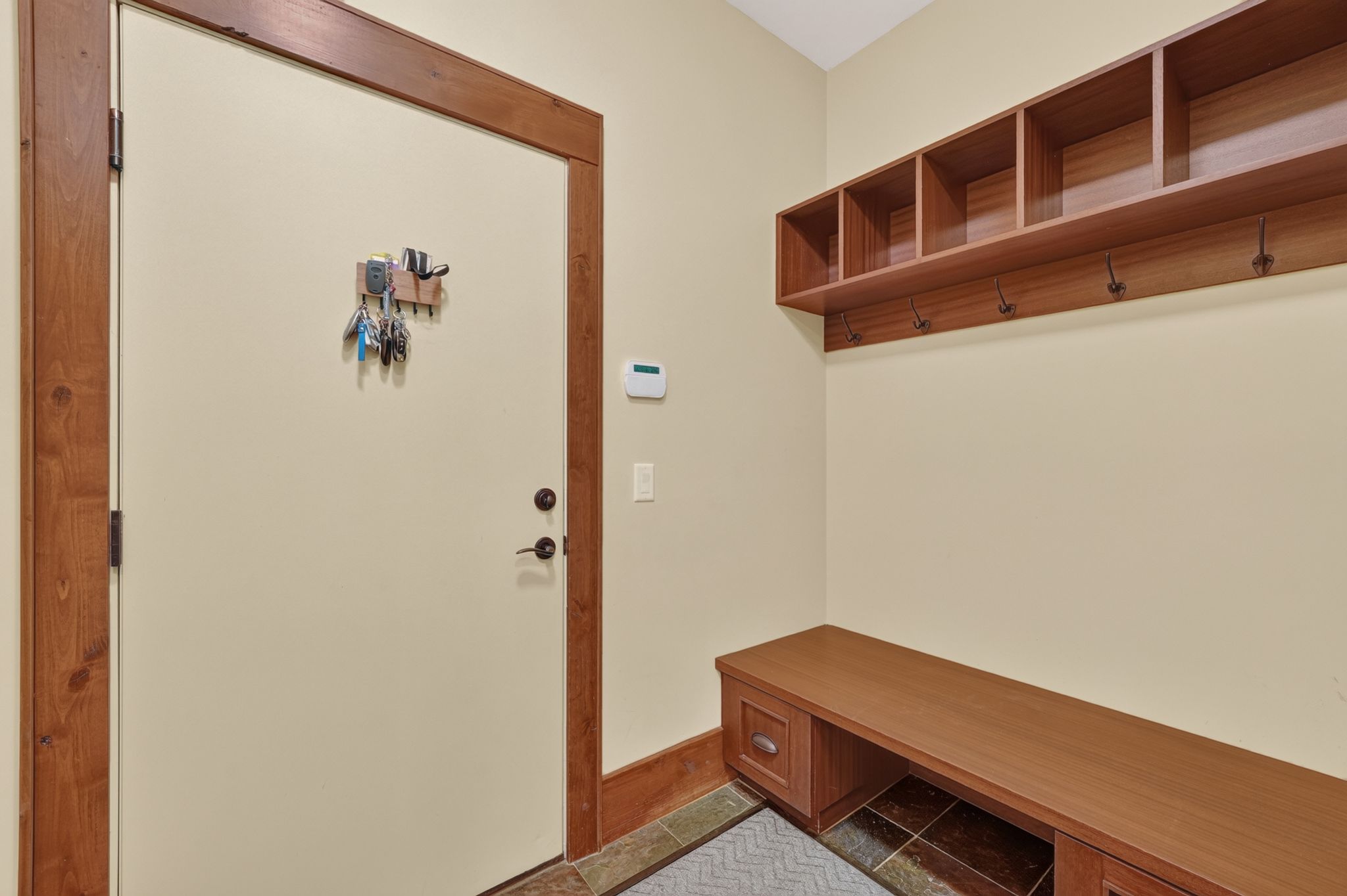 Entryway featuring a wood-finish door frame, built-in bench with storage, integrated shelving, coat hooks, and multi-tone tile flooring