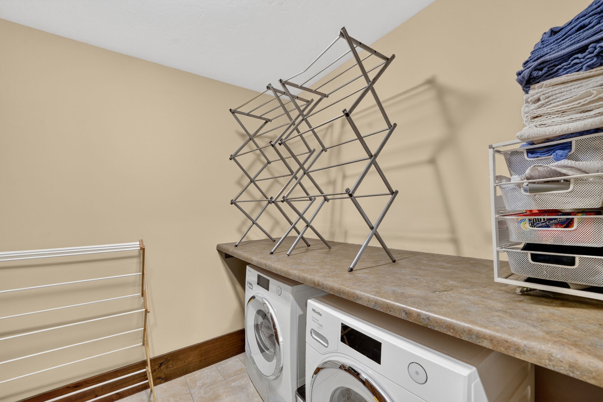 Laundry area featuring light beige walls, a built-in countertop, wood trim, and a textured ceiling