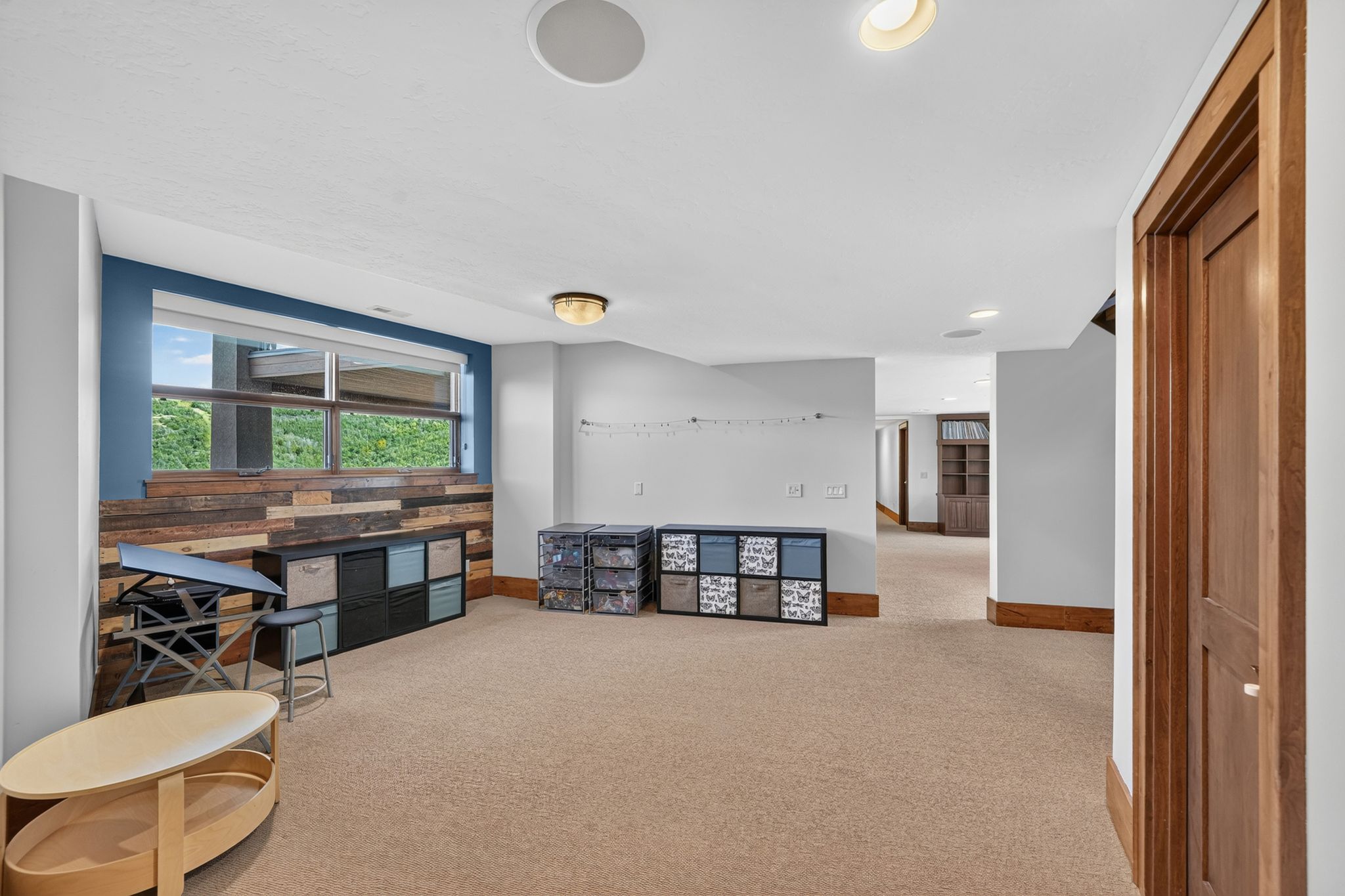 Spacious room featuring a large window, wood-paneled accent wall, and light-colored carpeting