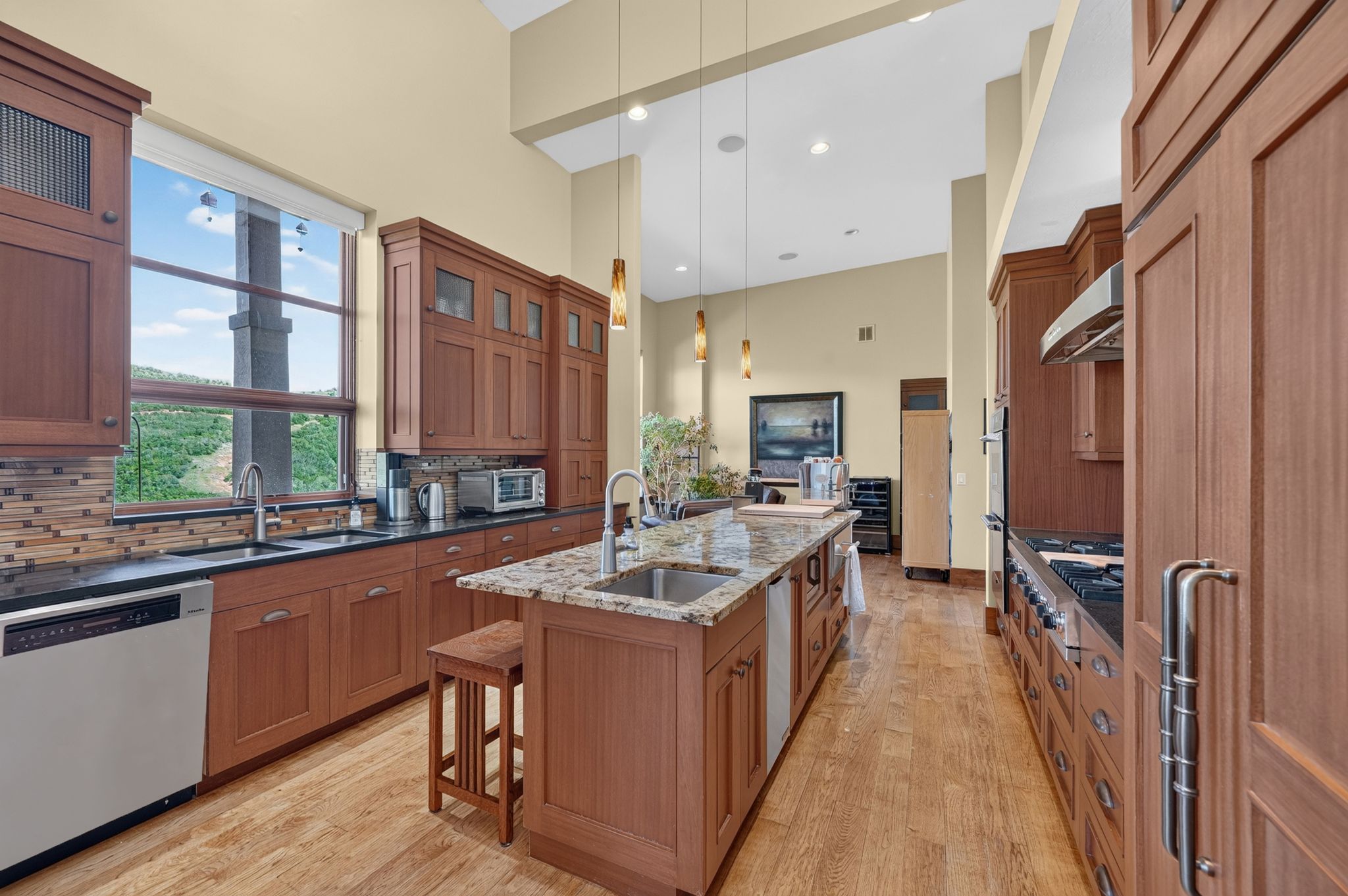 Gourmet kitchen featuring a large central island with integrated sink, extensive wood cabinetry, granite countertops, a full suite of stainless steel appliances, and wood-finish flooring