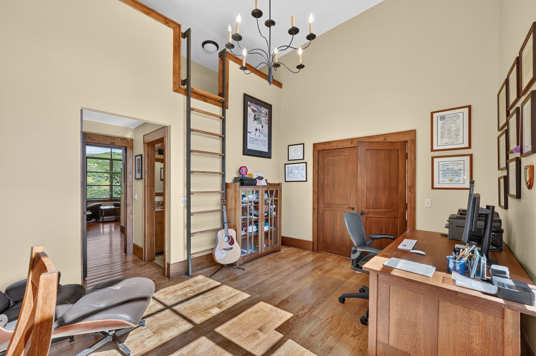 High-ceiling room featuring wood-finish flooring, a built-in ladder to an upper loft, and a dark-toned chandelier