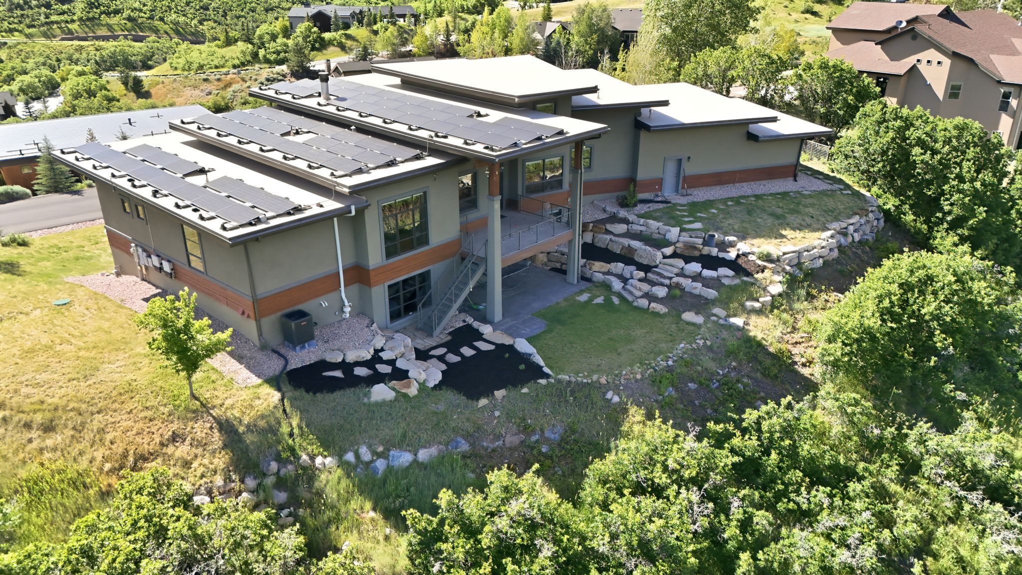 Contemporary residence featuring multiple solar panel arrays, a multi-level deck, and extensive rock landscaping